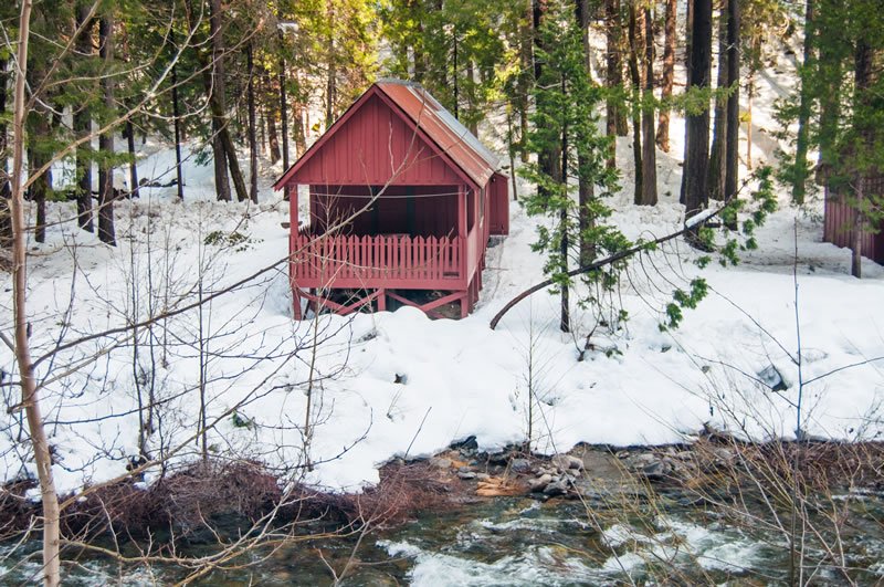 A red covered bridge over a creek in a snowy forest.