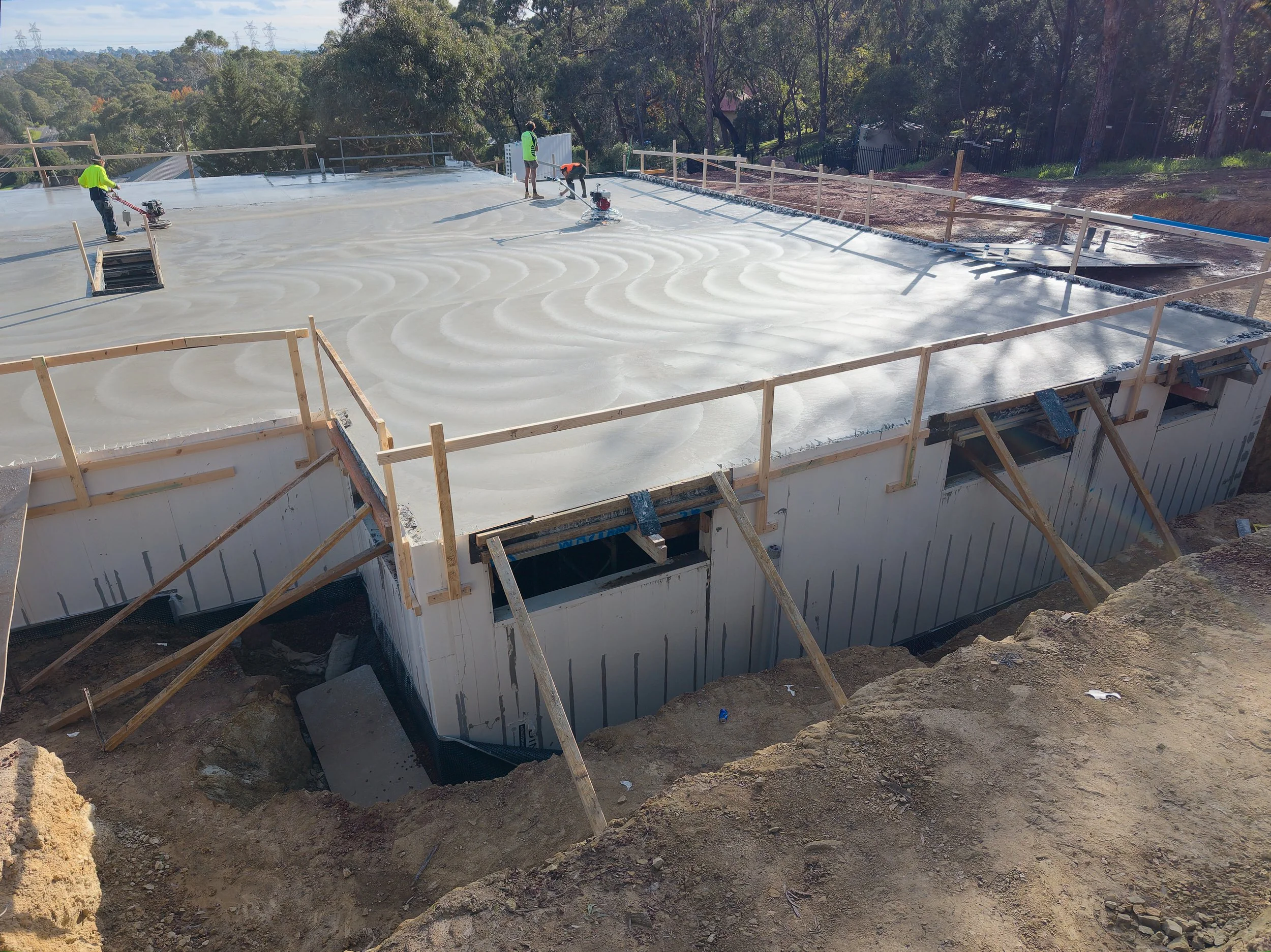 Workers smoothing wet concrete on a suspended slab at a construction site.