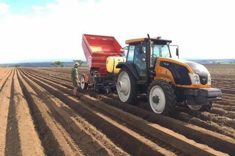 A Valtra in a field, with a person standing nearby.
