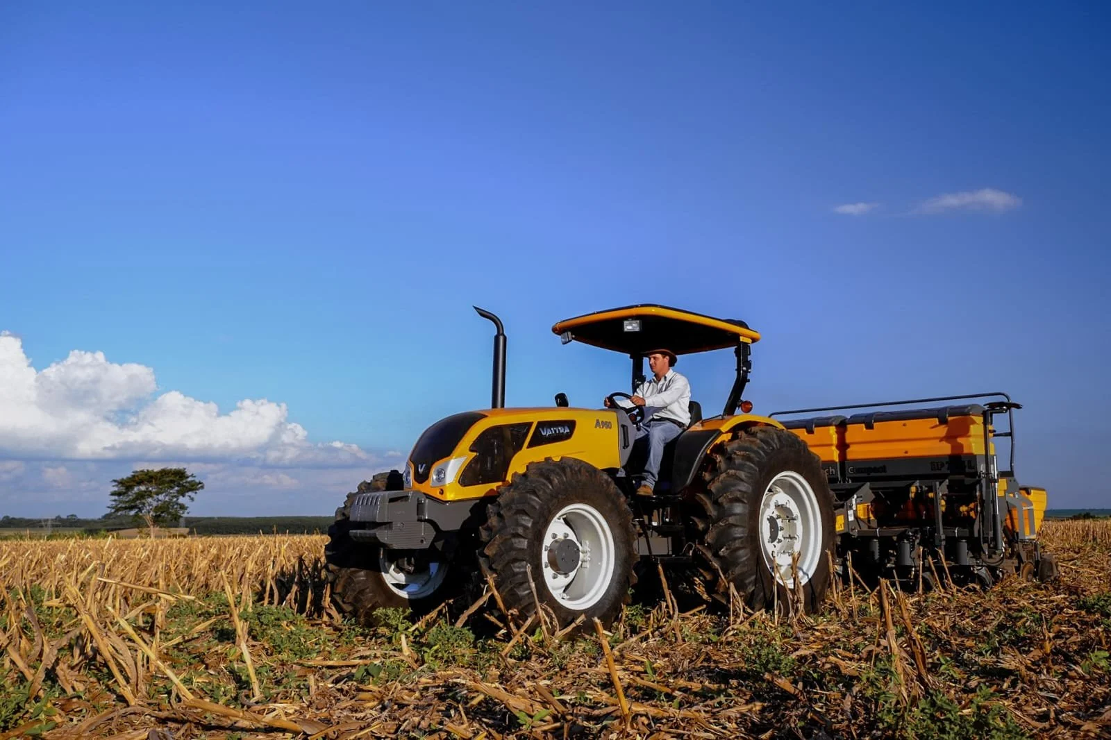 A man driving a Valtra in a cornfield under a blue sky with some clouds.