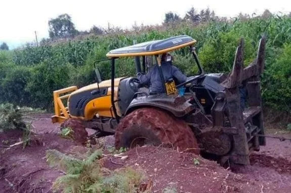 A Valtra in muddy soil in a field with green crops.