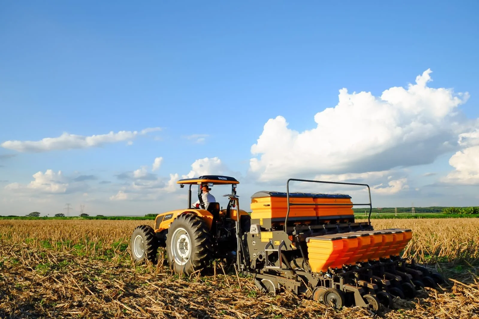 A farmer operating a Valtra in a field during daytime with a partly cloudy sky.