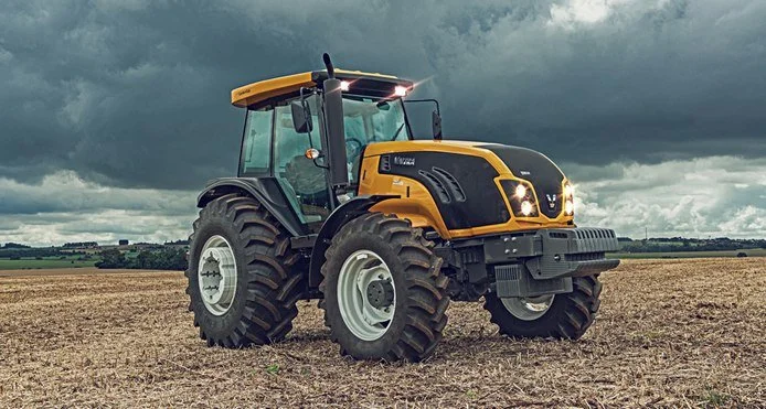 Yellow and blackValtra in an open field under cloudy sky.