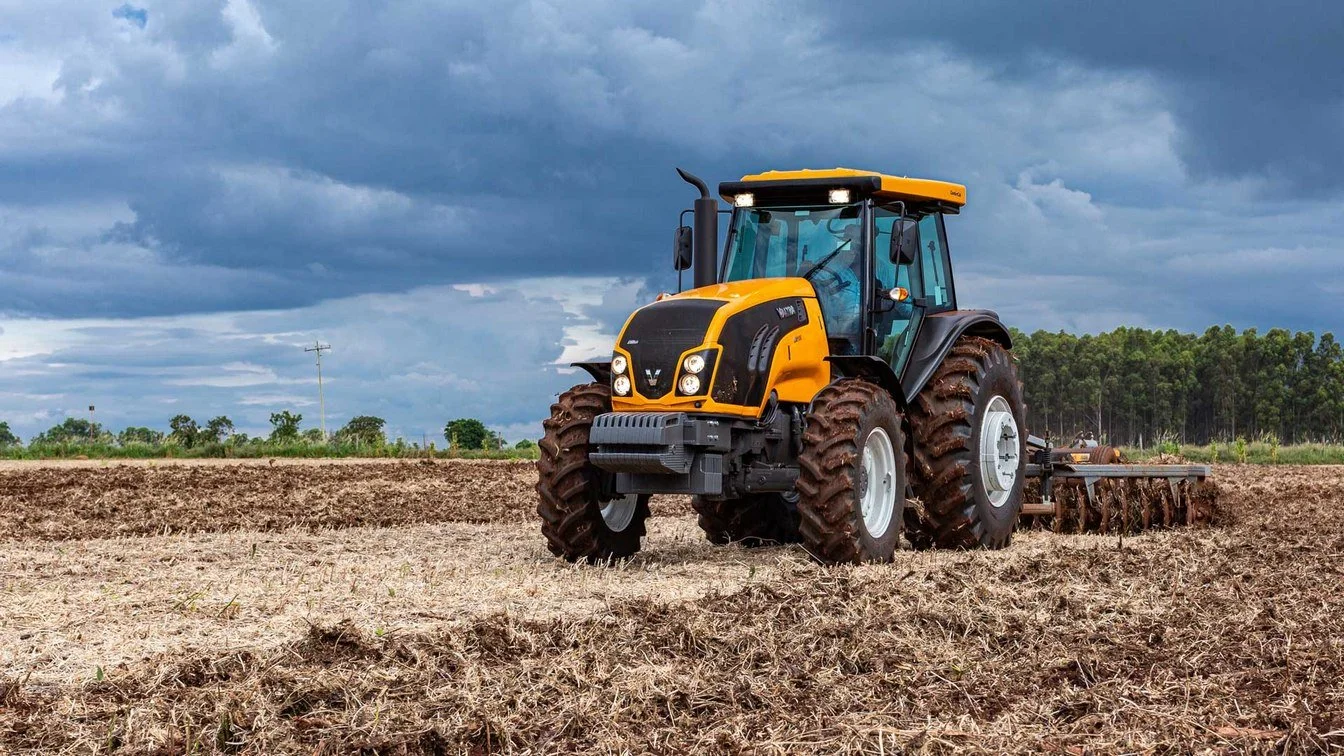 A yellow and black Valtra tilling a field under a cloudy sky.