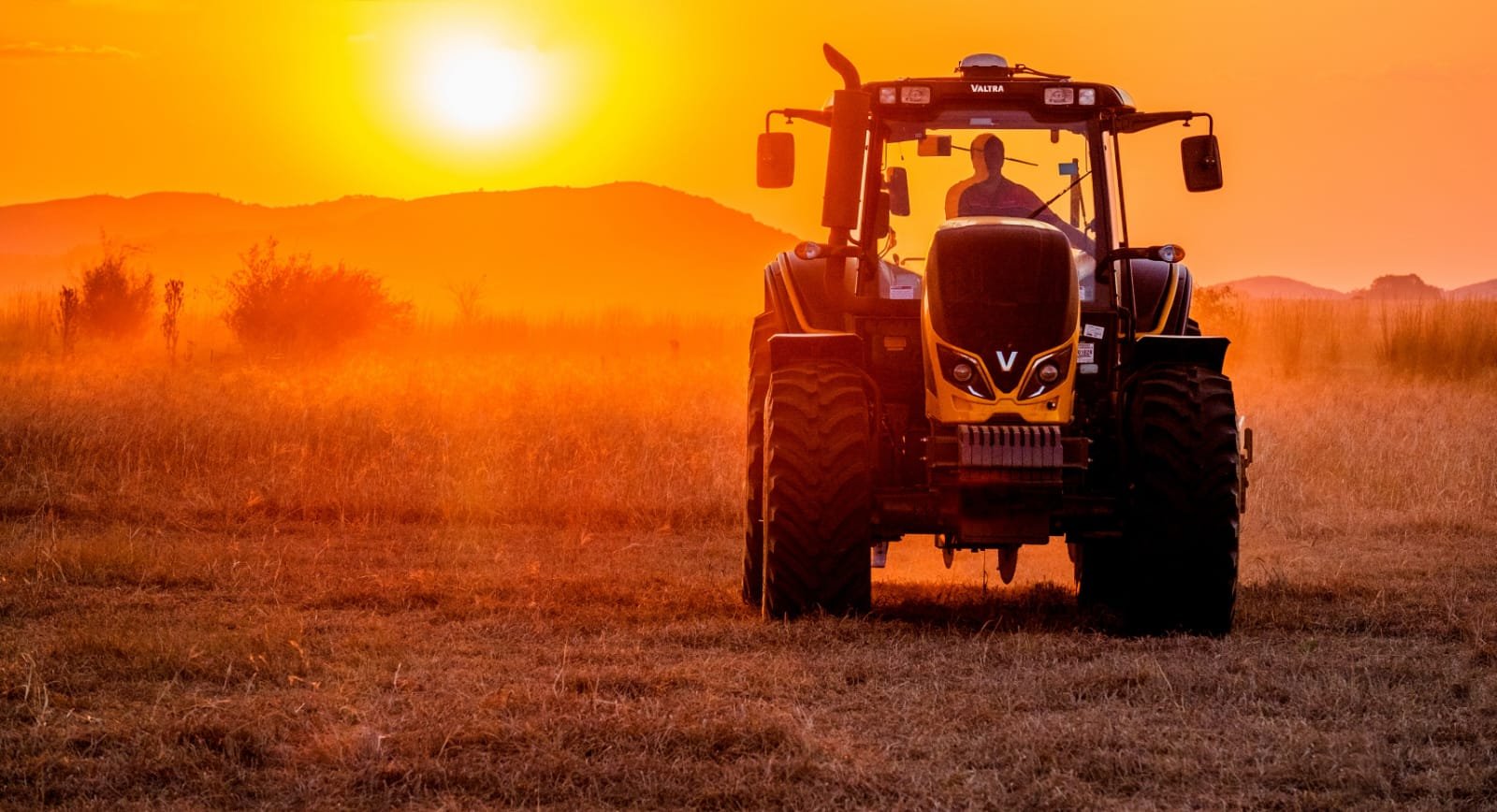 A Valtra driving across a field at sunset with hills in the background.