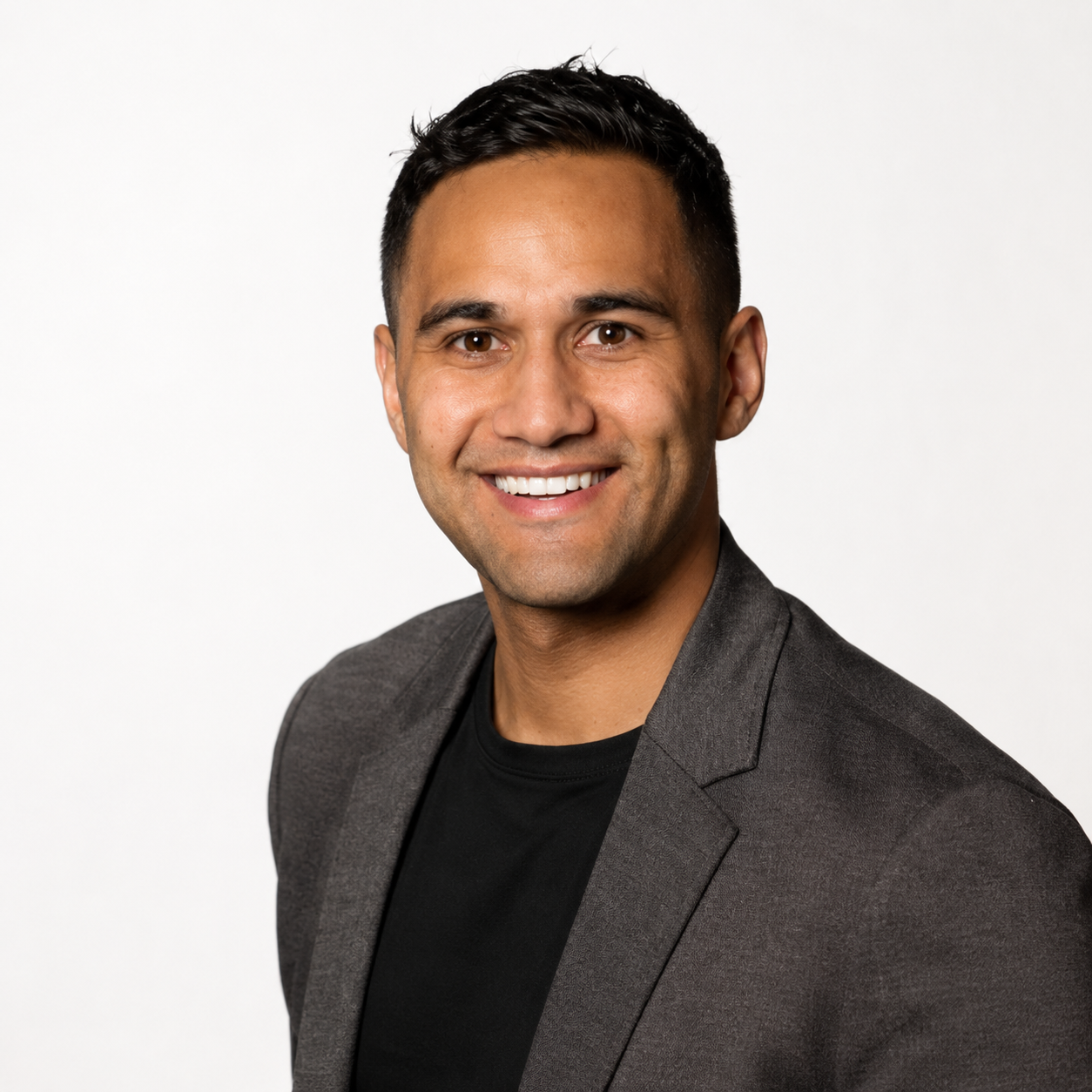 Professional headshot of a smiling man in a dark blazer and black shirt, facing forward against a white background.