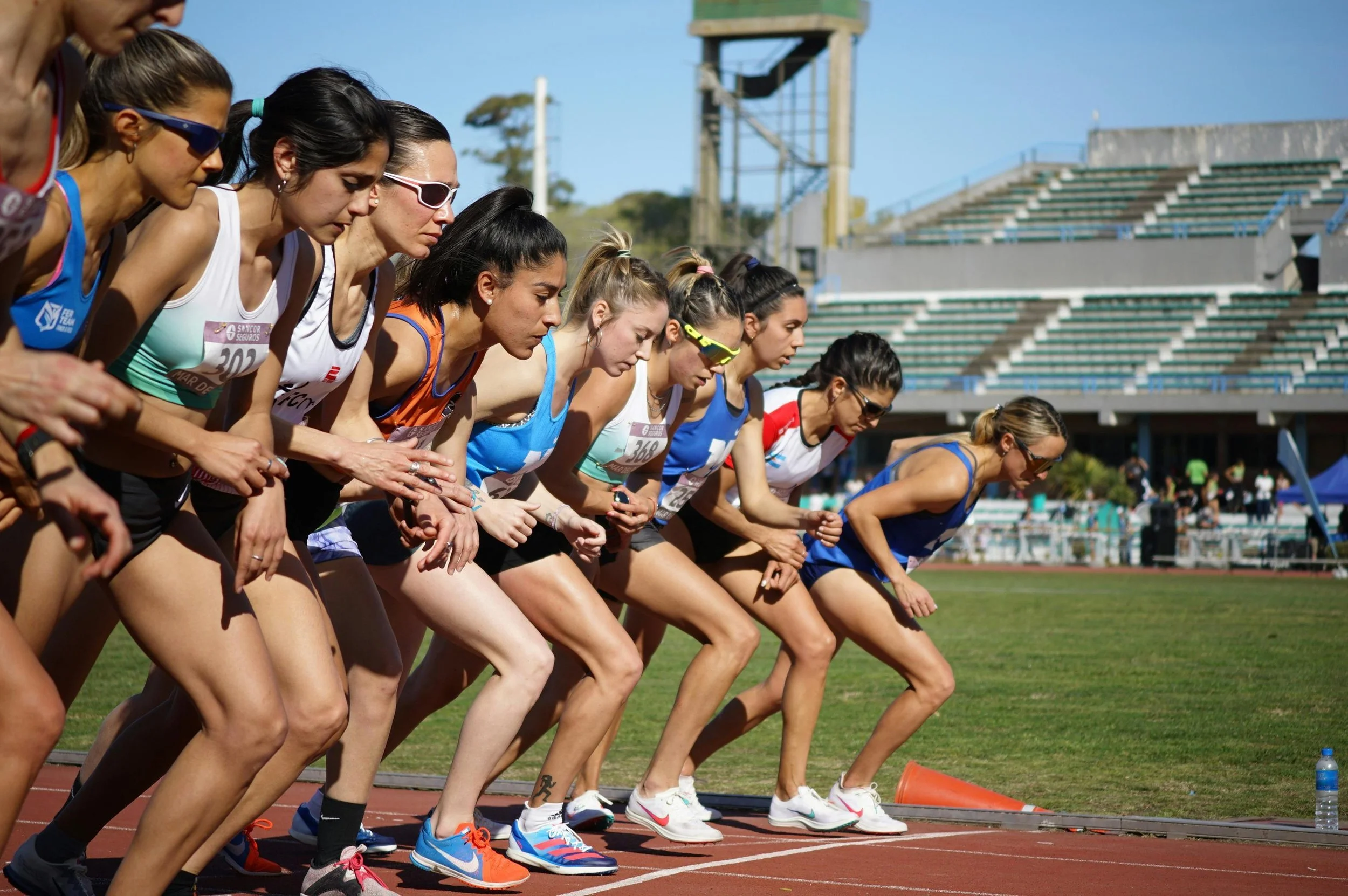 A line of women athletes at the start of a track race, poised to run.