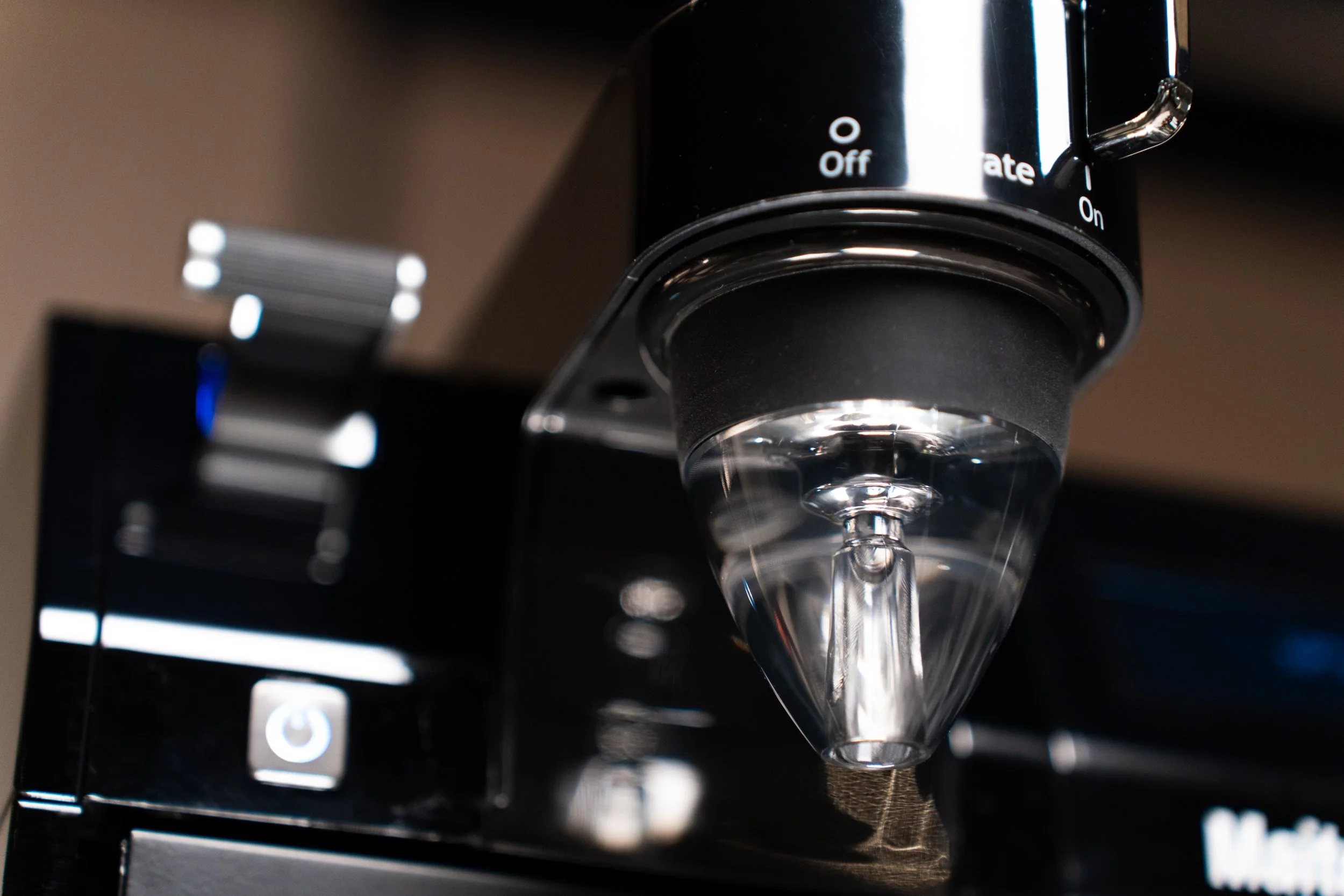 Close-up of a coffee machine's portafilter with a clear view of the spout, surrounded by buttons labeled with power symbols and switches marked 'Off' and 'On'.