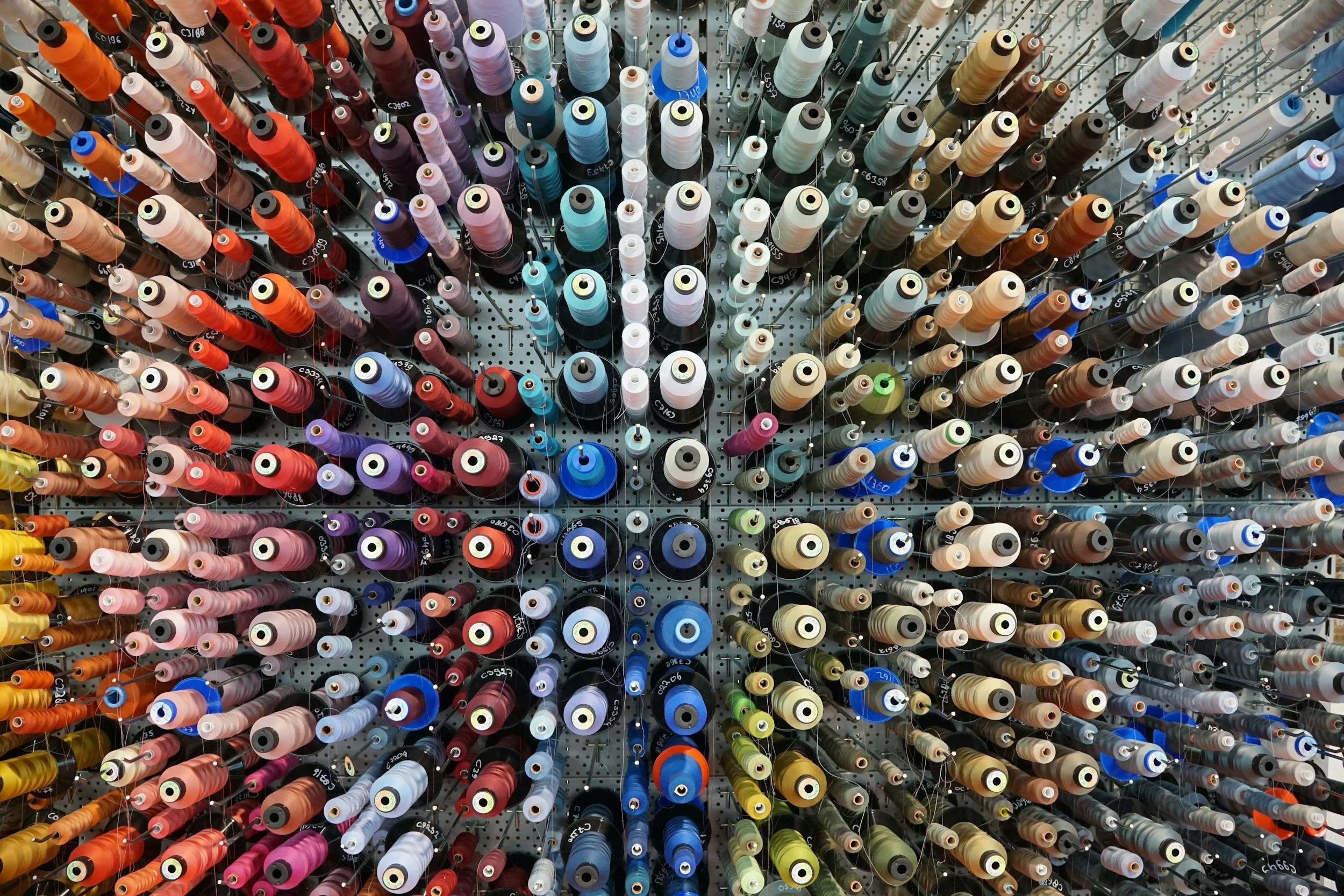 A display of colorful sewing thread spools arranged on a pegboard.