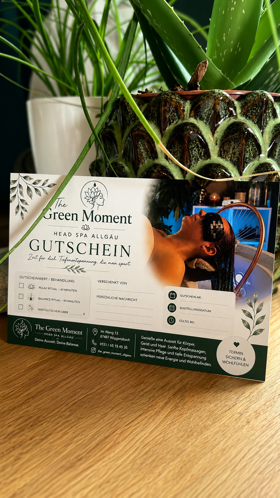 Ein Gutschein für eine Massage im Spa, mit einem Bild einer Frau beim Entspannen, Pflanzen im Hintergrund und einer Hautpflegebehandlung im Spa. Der Gutschein ist auf einem Holztisch platziert.