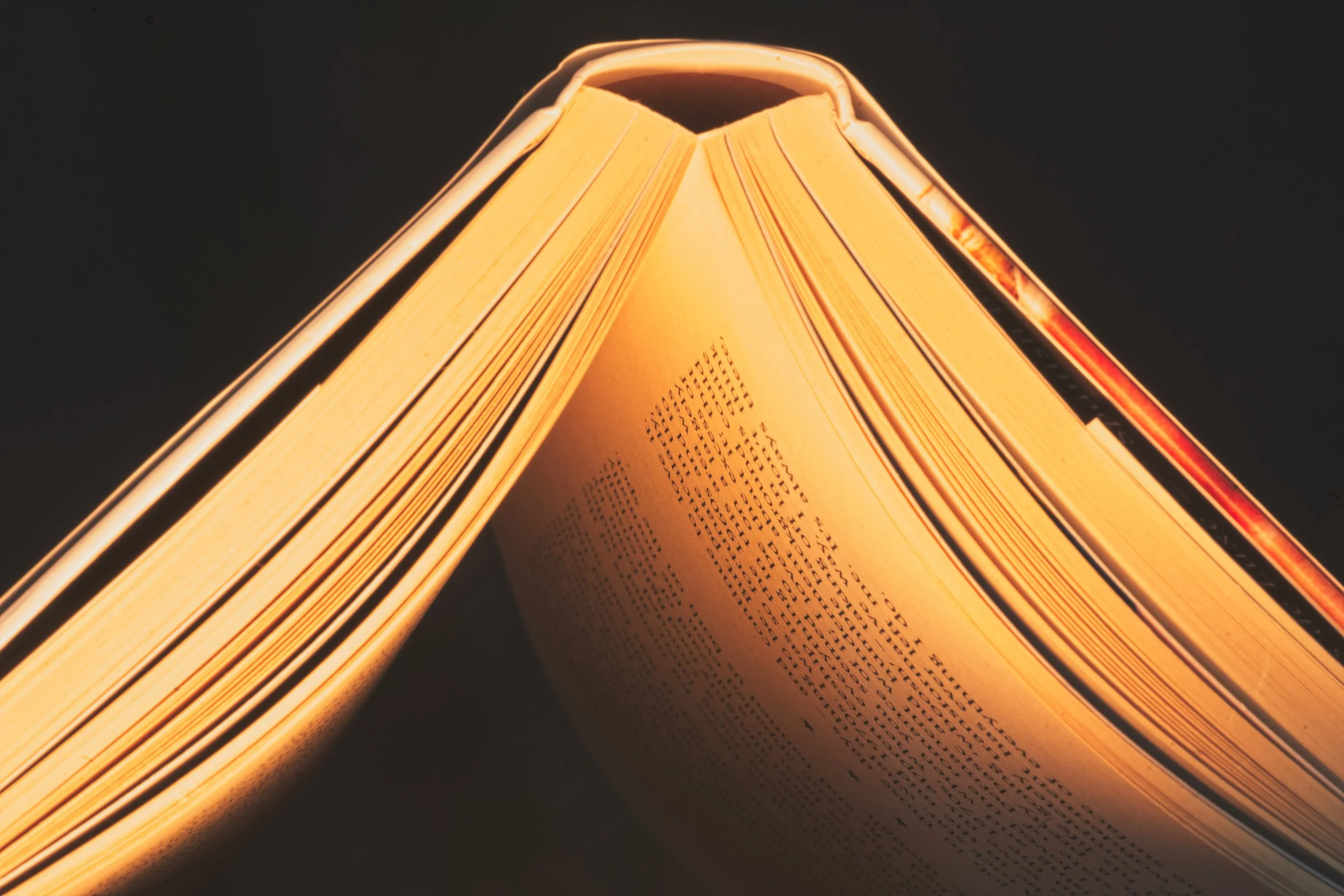 A close-up view of an open book with pages glowing under warm light, against a dark background. Photography by photographer based in Southam, Warwickshire