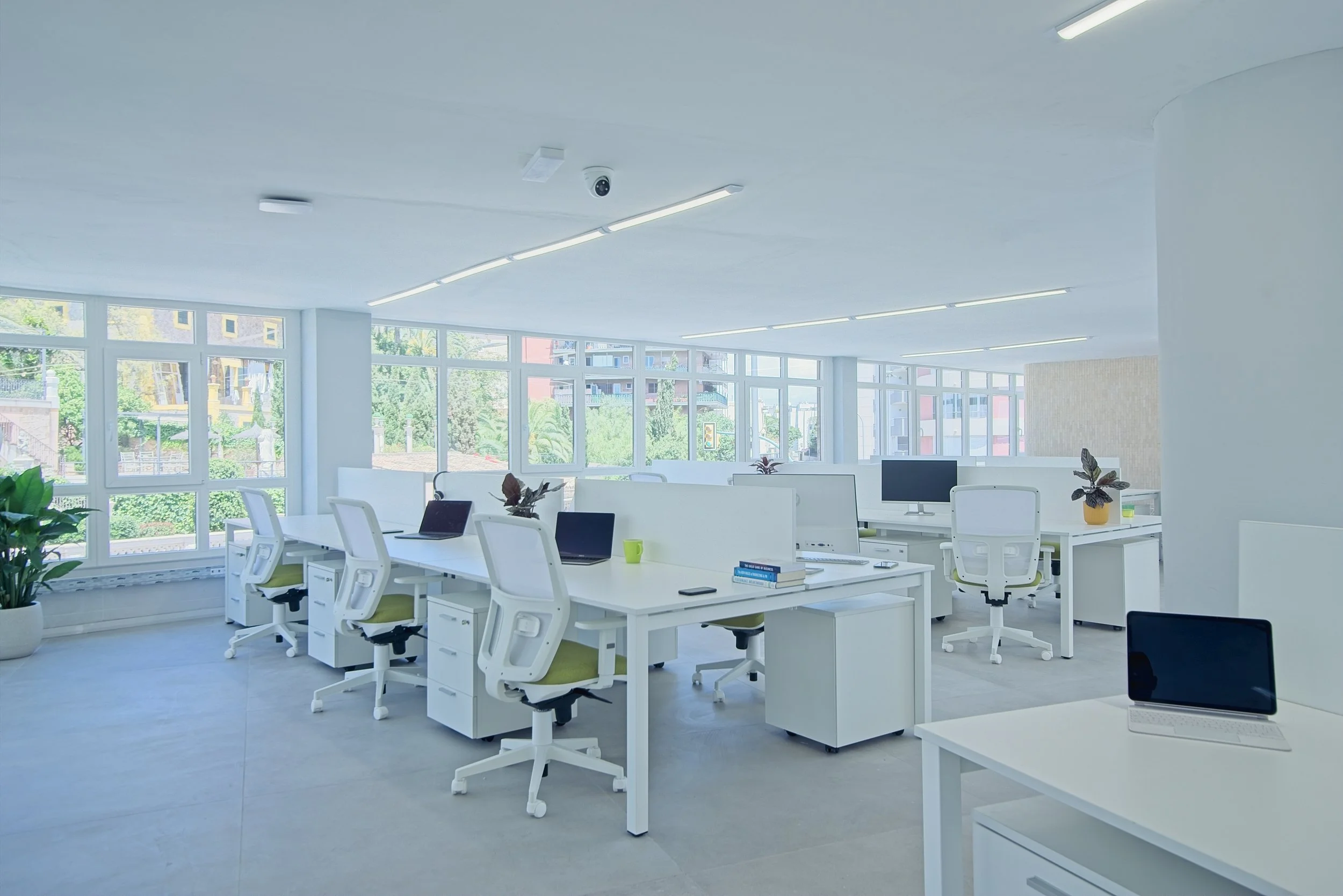 Modern office space with white desks, green chairs, laptops, and plants, illuminated by large windows and overhead lighting. Real estate and corporate photography Warwickshire.