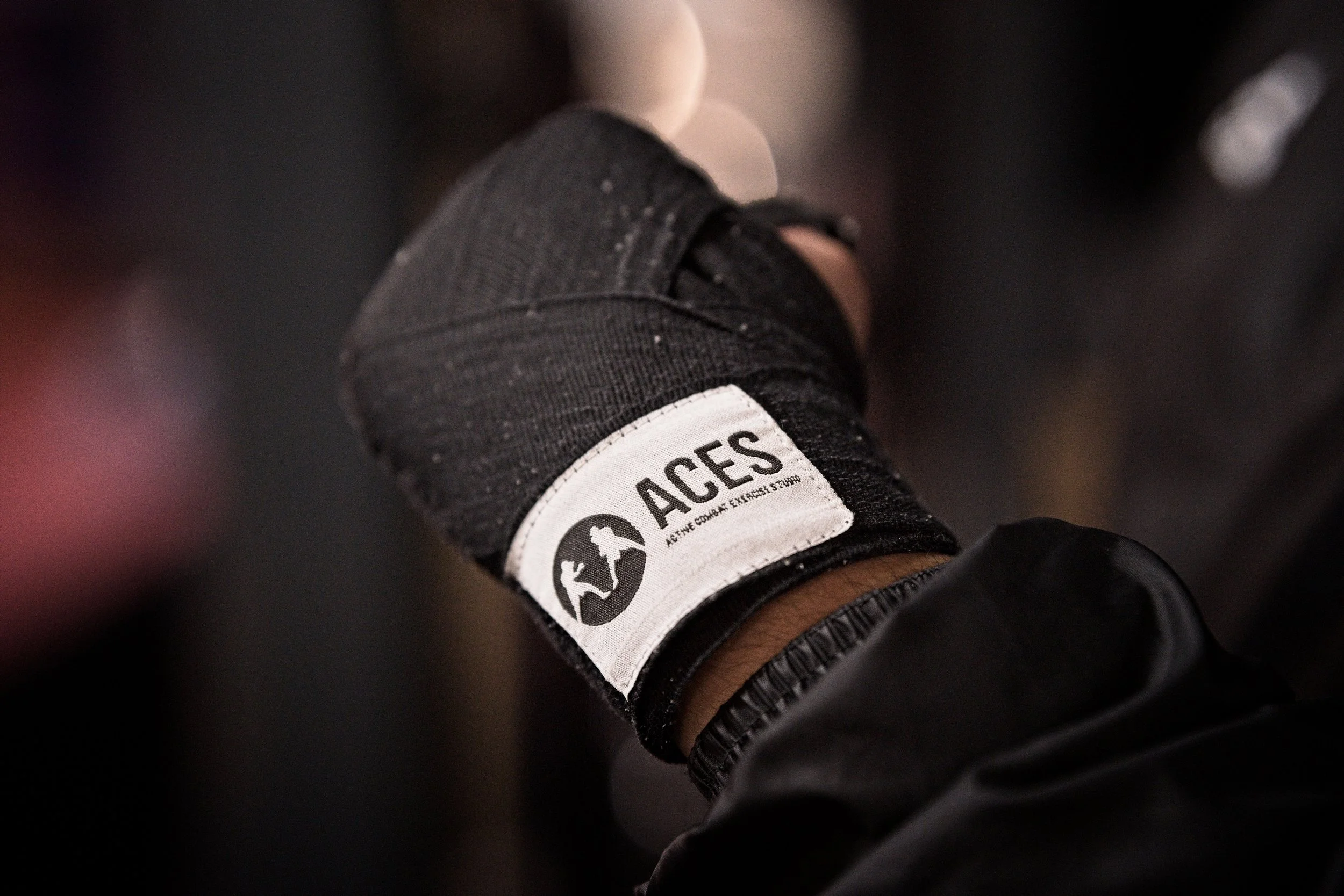A close-up of a person's hand wearing a black workout glove with a white logo patch that reads 'ACES' and features icons of a person lifting a dumbbell and a person running. Warwickshire sports photography.