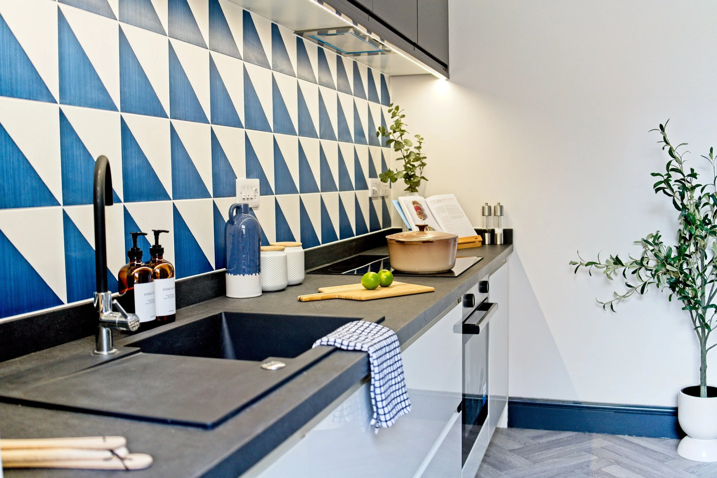 Modern kitchen with a dark countertop, a black sink, and a blue and white geometric tile backsplash. Property Photography by photographer based in Southam, Warwickshire
