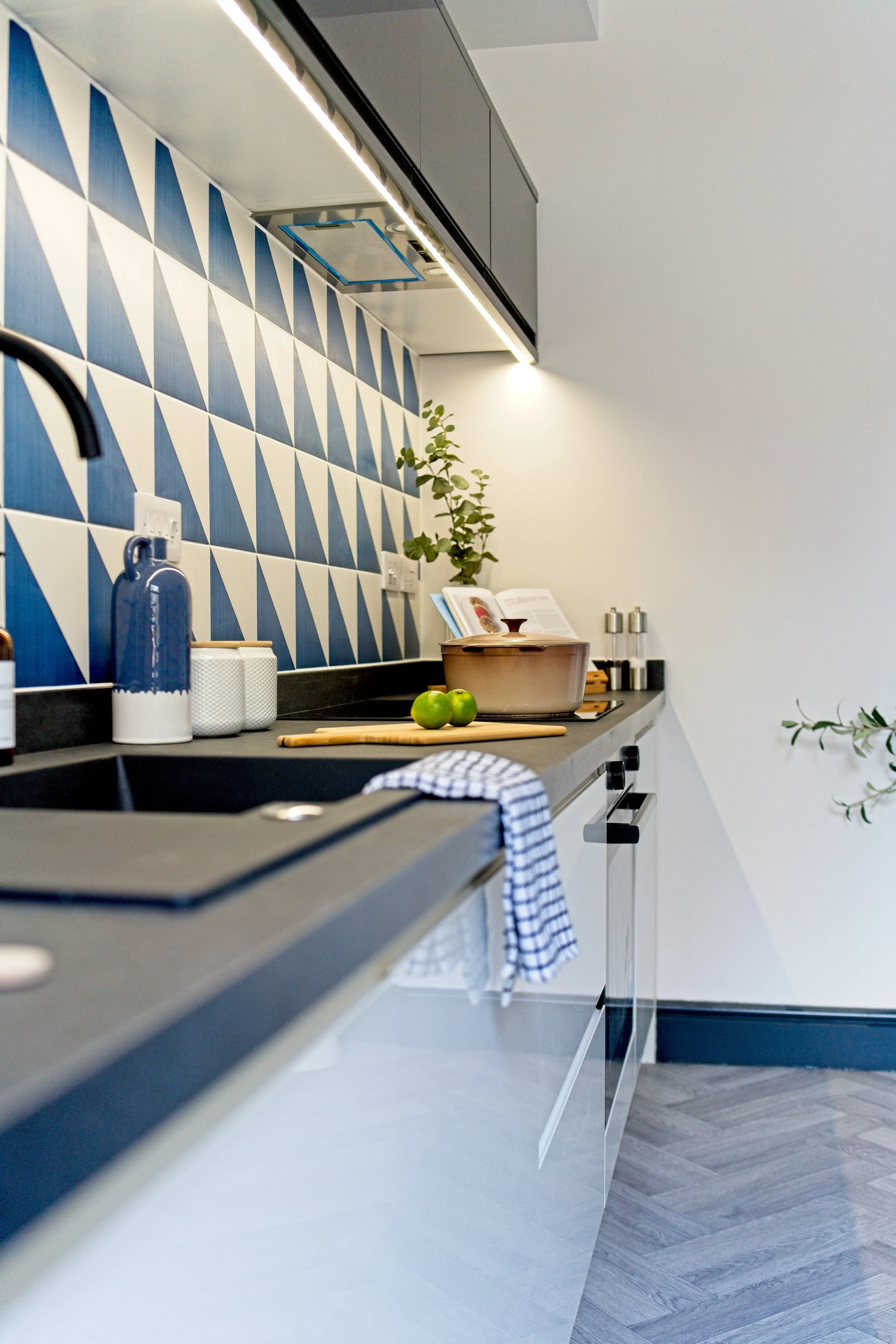 Modern kitchen with black countertop, blue and white geometric tile backsplash, and various kitchen items including a pot, limes, and glass containers. Property Photography by photographer based in Southam, Warwickshire
