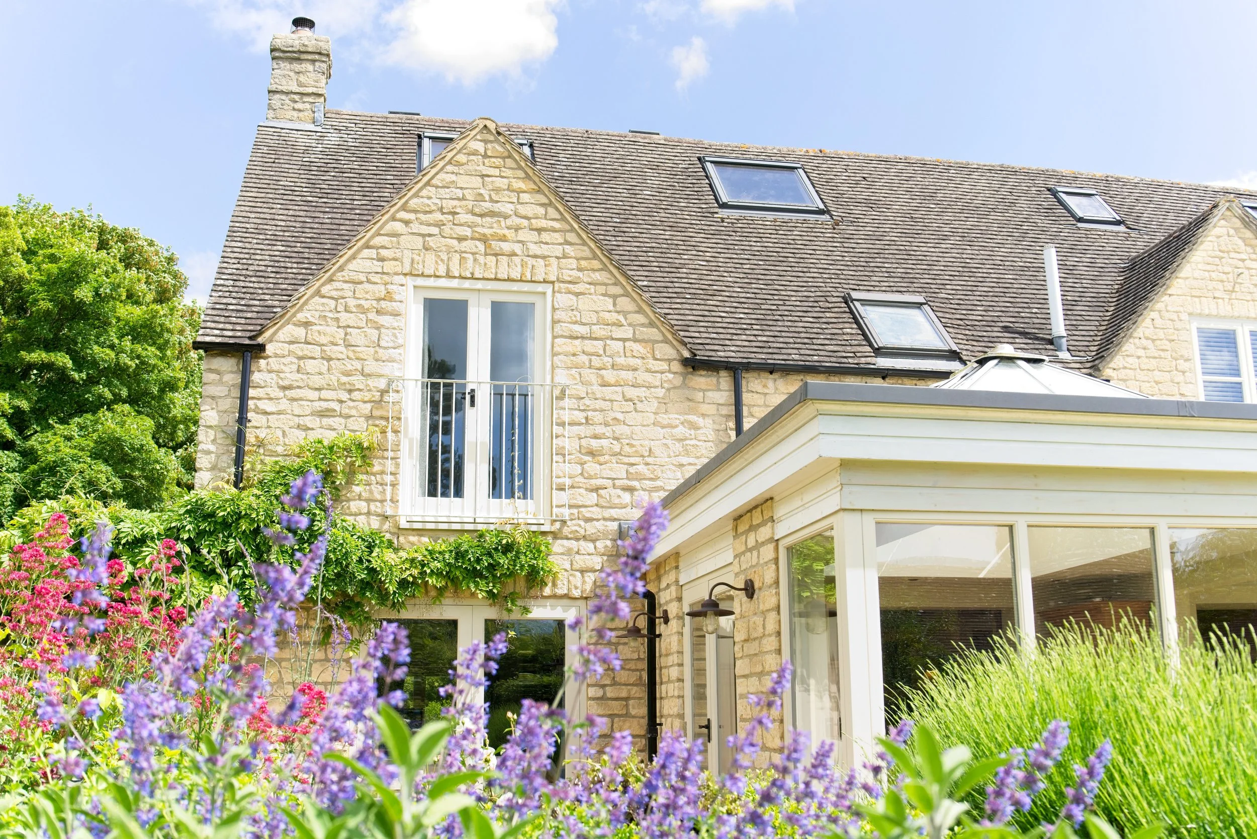 A house with a stone exterior, multiple skylights, and a garden with purple and pink flowers. Property photography by photographer based in Southam, Warwickshire