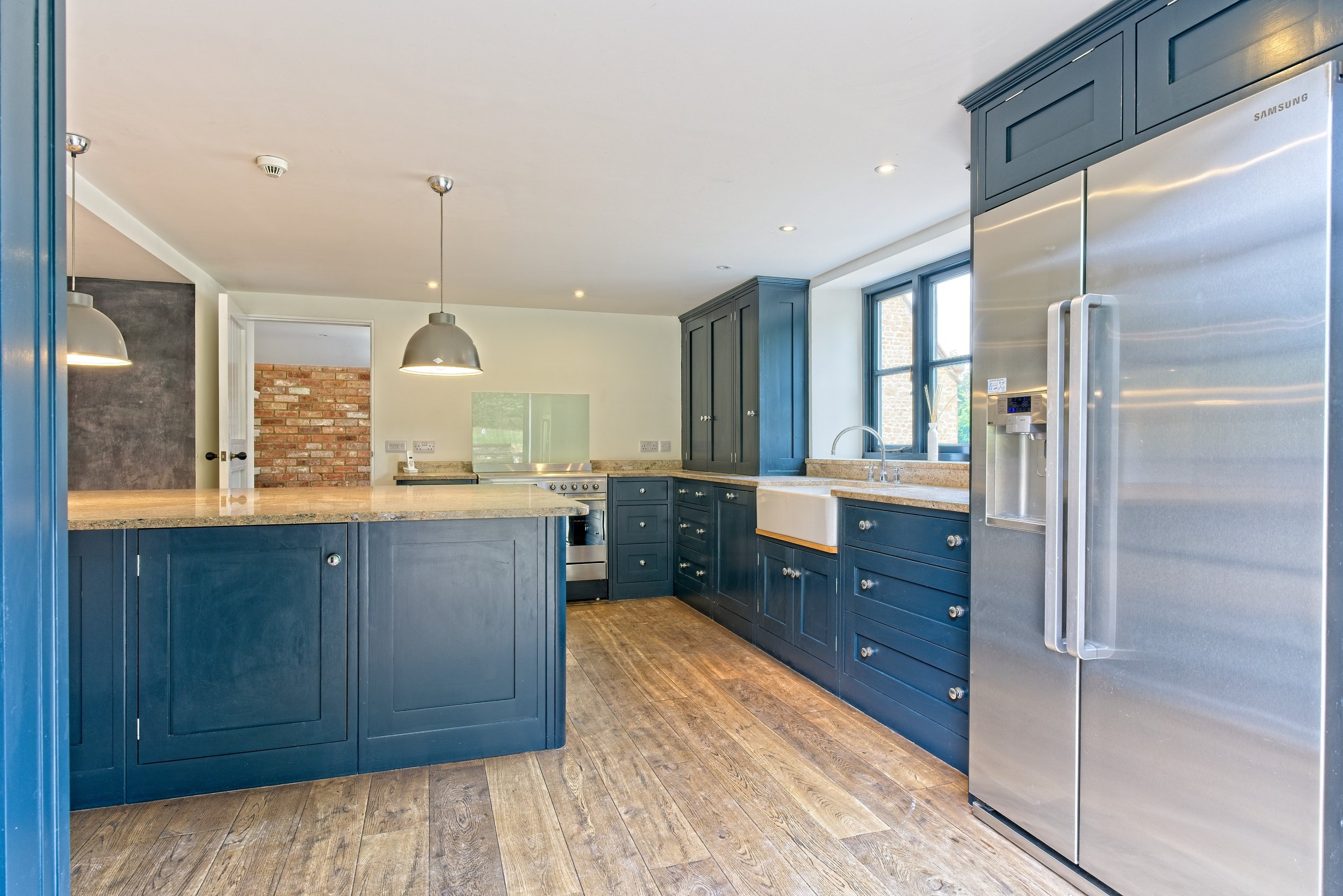 Modern kitchen with blue cabinets, stainless steel appliances, wooden flooring, and a large window. Photography by photographer based in Southam, Warwickshire