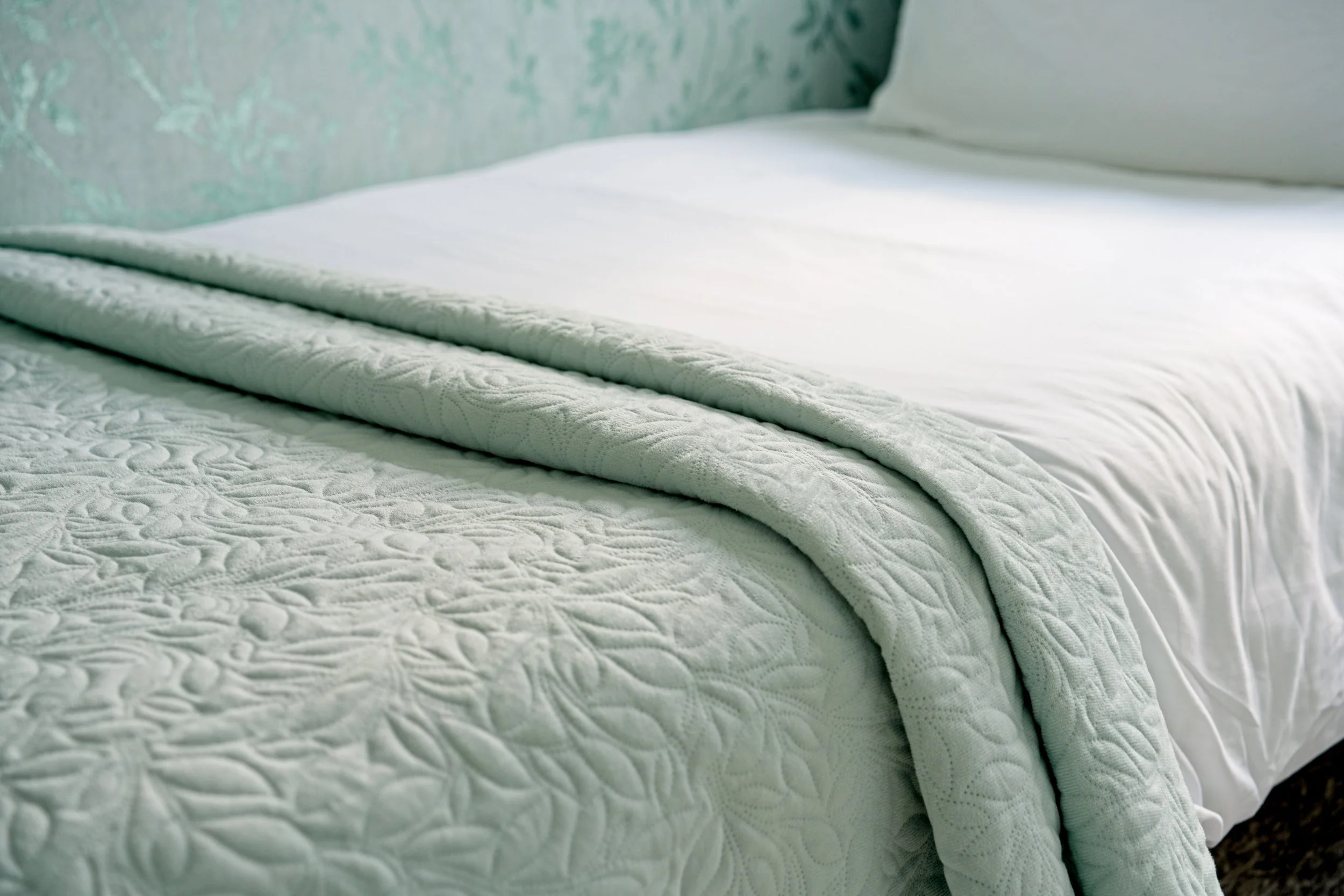 Close-up of a neatly made bed with a white quilted blanket and pillow against a patterned wall. Property Photography by photographer based in Southam, Warwickshire