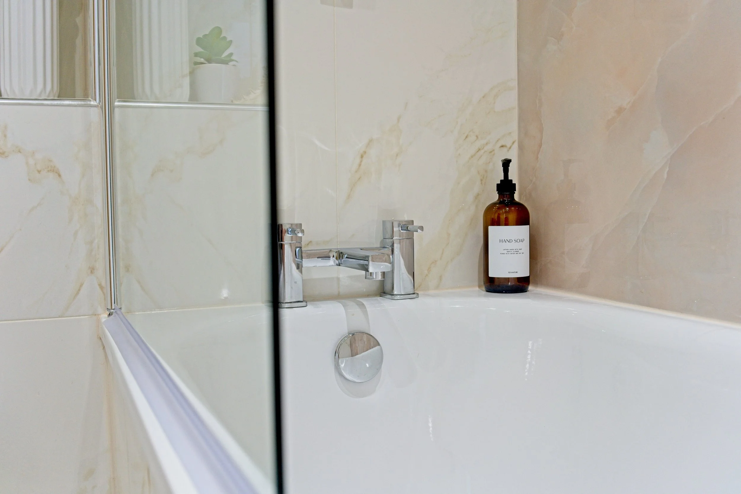 Bathroom sink with chrome faucet and amber soap dispenser labeled 'HAND SOAP' on a beige marble wall. Photography by photographer based in Southam, Warwickshire