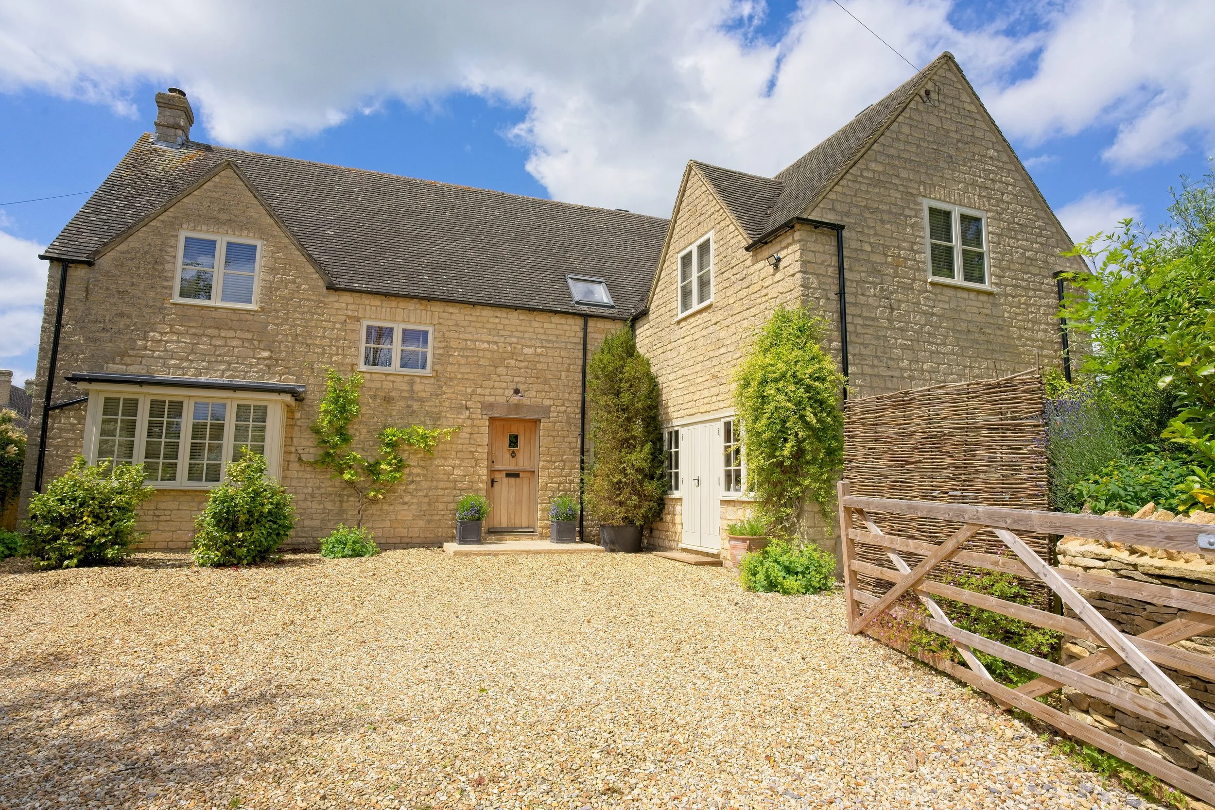 Cottage with stone walls, pitched roof, and a gravel driveway, with potted plants and greenery in front. Property photography by photographer based in Southam, Warwickshire