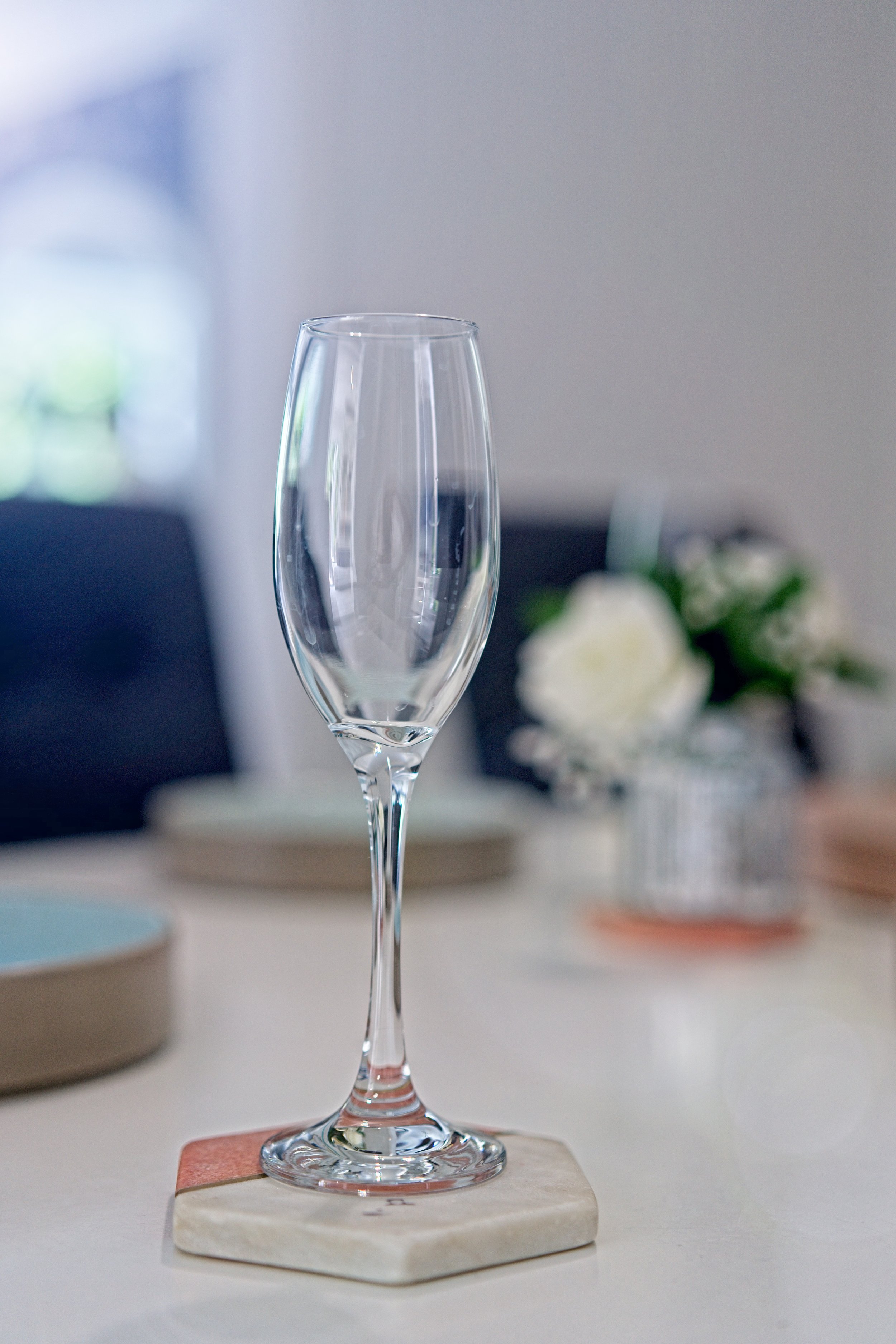 Close-up of an empty champagne flute glass on a cork coaster on a dining table with blurred background of white flowers and dishes. Property Photography by photographer based in Southam, Warwickshire