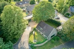 Aerial view of a residential neighborhood with a white house, surrounded by trees and greenery, with neighboring houses visible in the background. Real estate photography in the Cotswolds and Warwickshire.