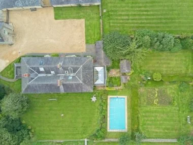 Aerial view of a house with a backyard, swimming pool, garden, and surrounding greenery. Real estate photography in the Cotswolds and Warwickshire.