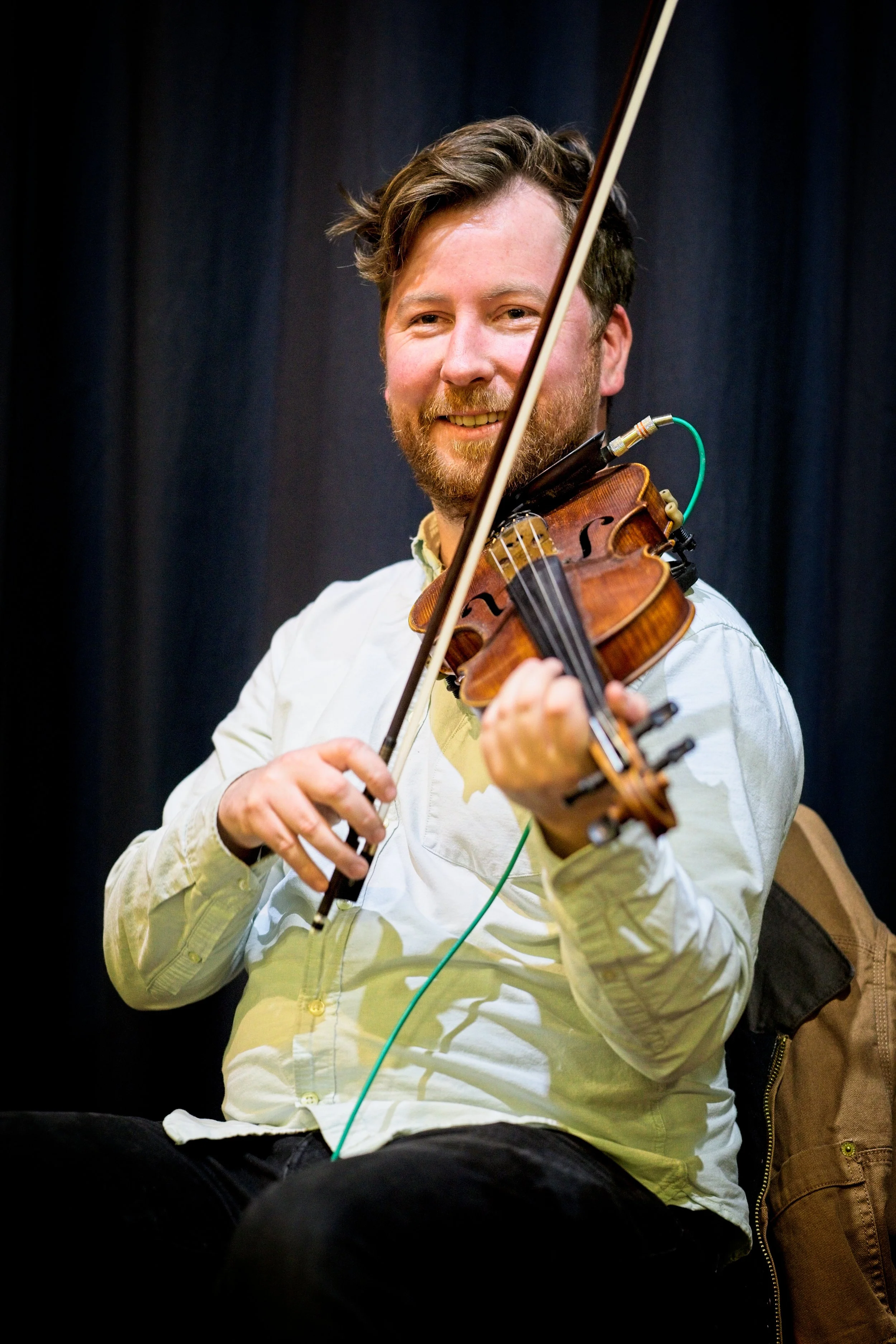 A man with a beard and wavy hair playing a violin and smiling at the camera. Event Photography by photographer based in Southam, Warwickshire