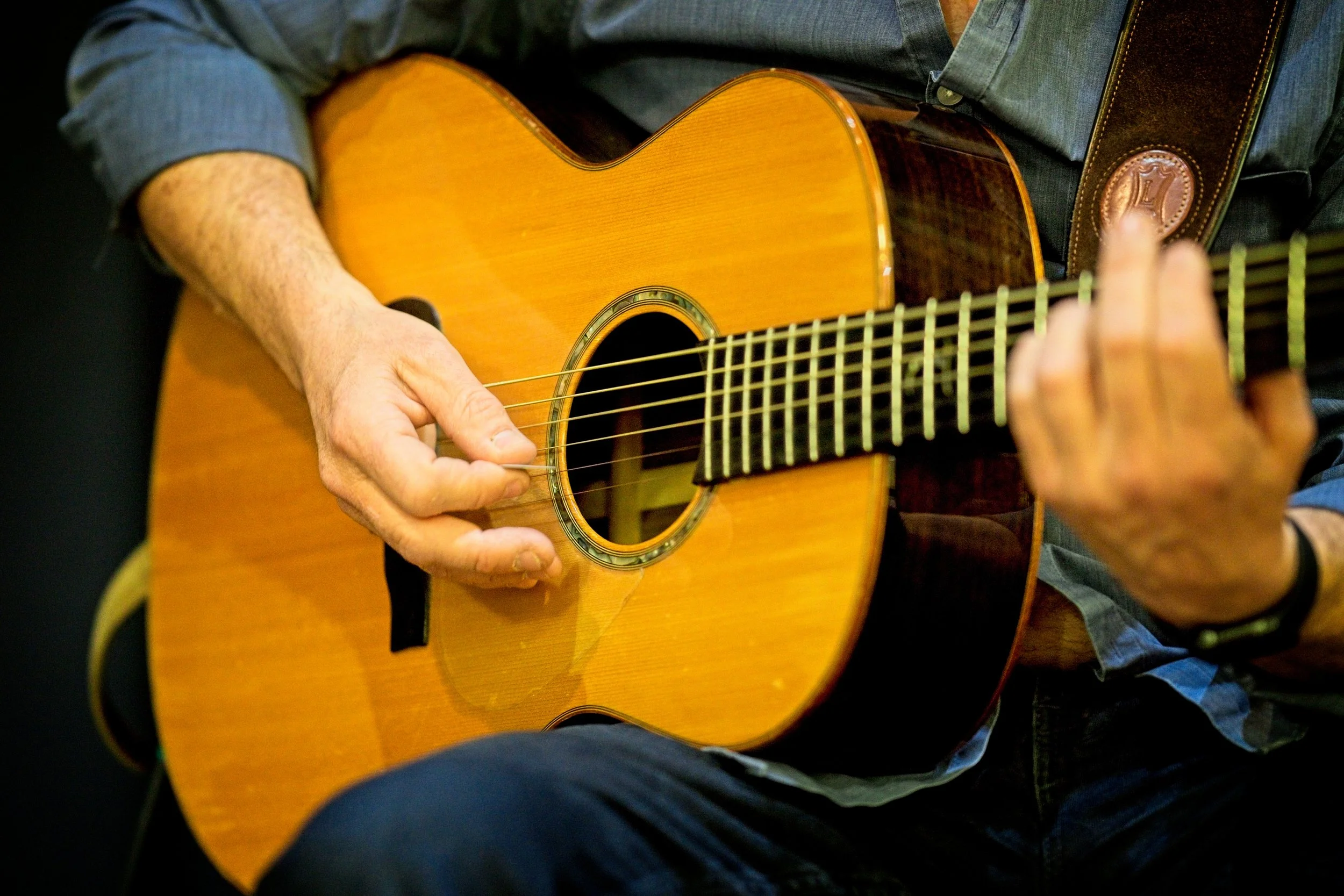 A person playing an acoustic guitar, with focus on their hand strumming the strings and their other hand pressing on the frets. Event Photography by photographer based in Southam, Warwickshire