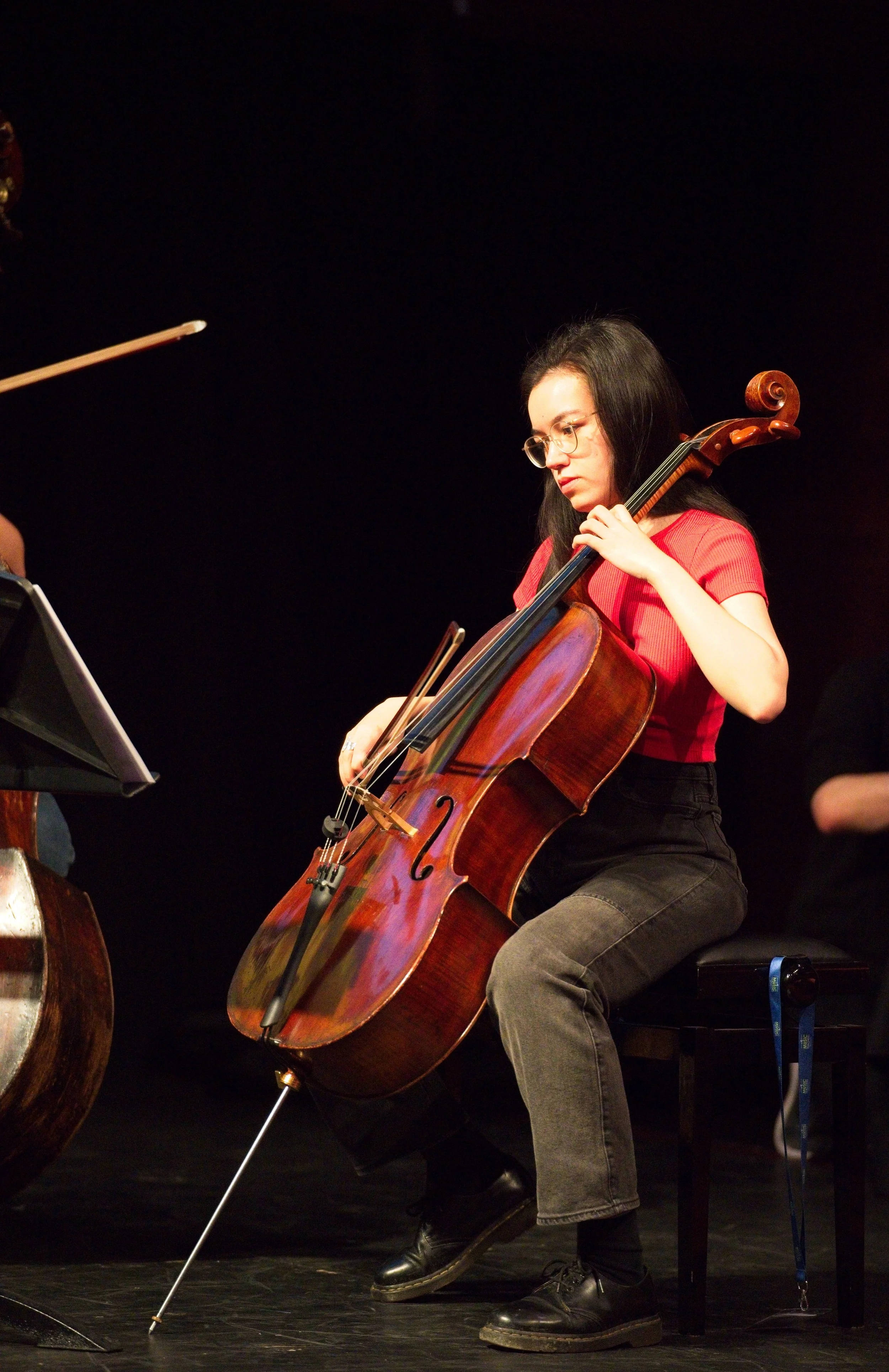 A woman with long dark hair and glasses playing a cello during a performance. Event Photography by photographer based in Southam, Warwickshire