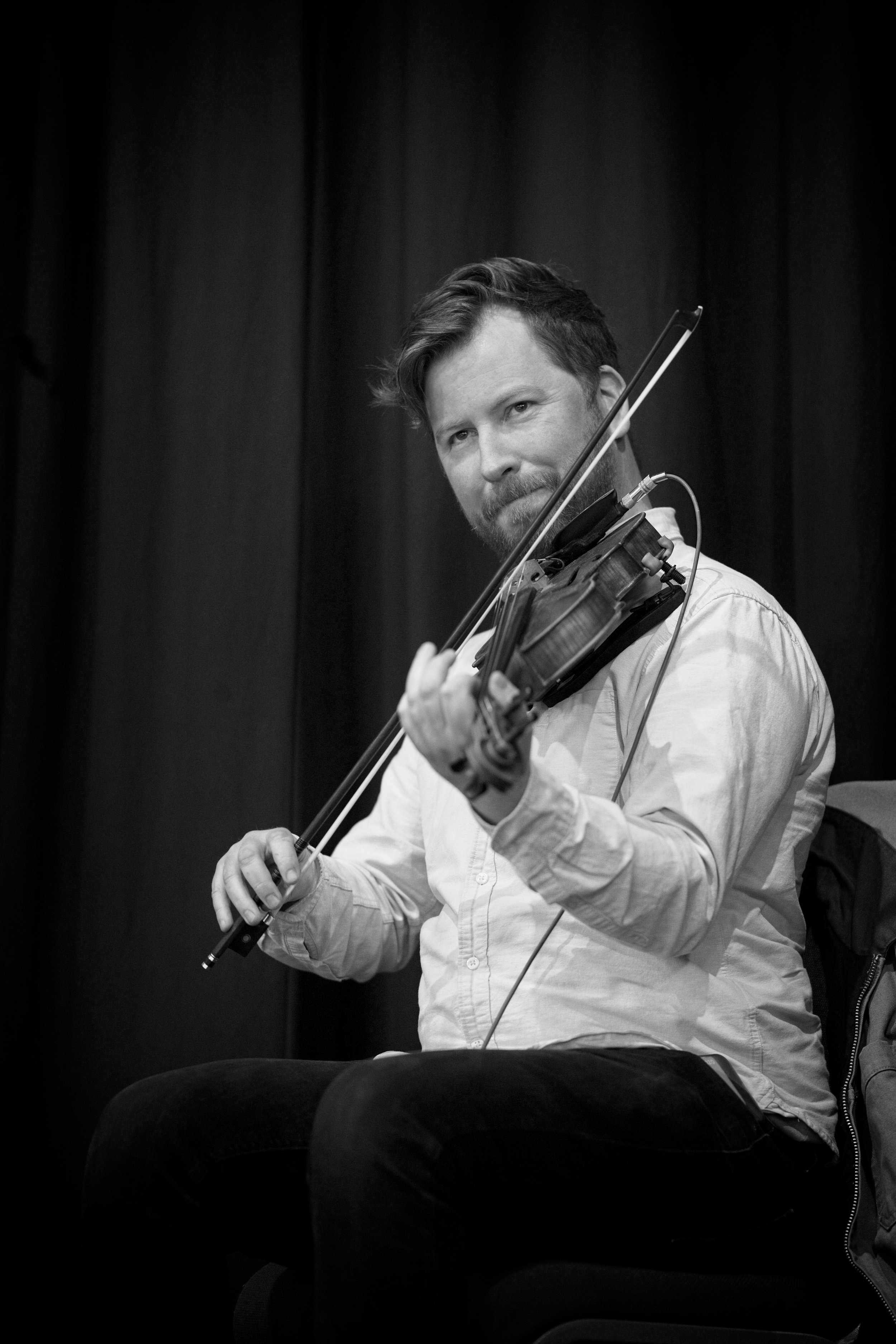 A man playing an electric violin in a studio or performance space, looking focused, with a dark curtain background. Event Photography by photographer based in Southam, Warwickshire