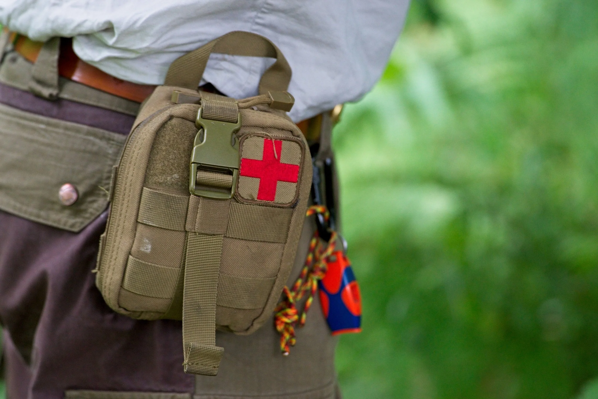A person wearing a khaki backpack with a red cross patch, standing outdoors with a blurred green background. Event Photography by photographer based in Southam, Warwickshire.