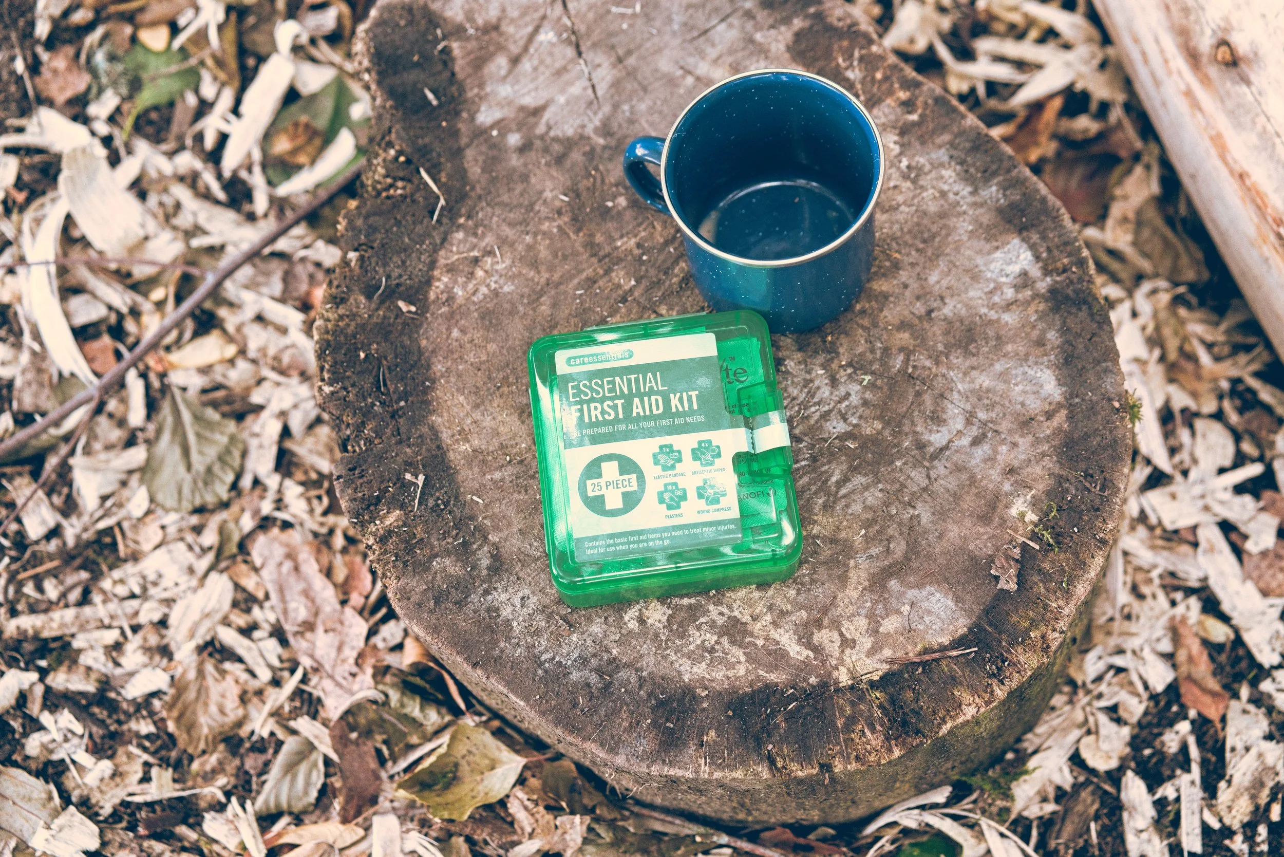 A blue mug and a green first aid kit on a tree stump surrounded by fallen leaves. Event Photography by photographer based in Southam, Warwickshire.