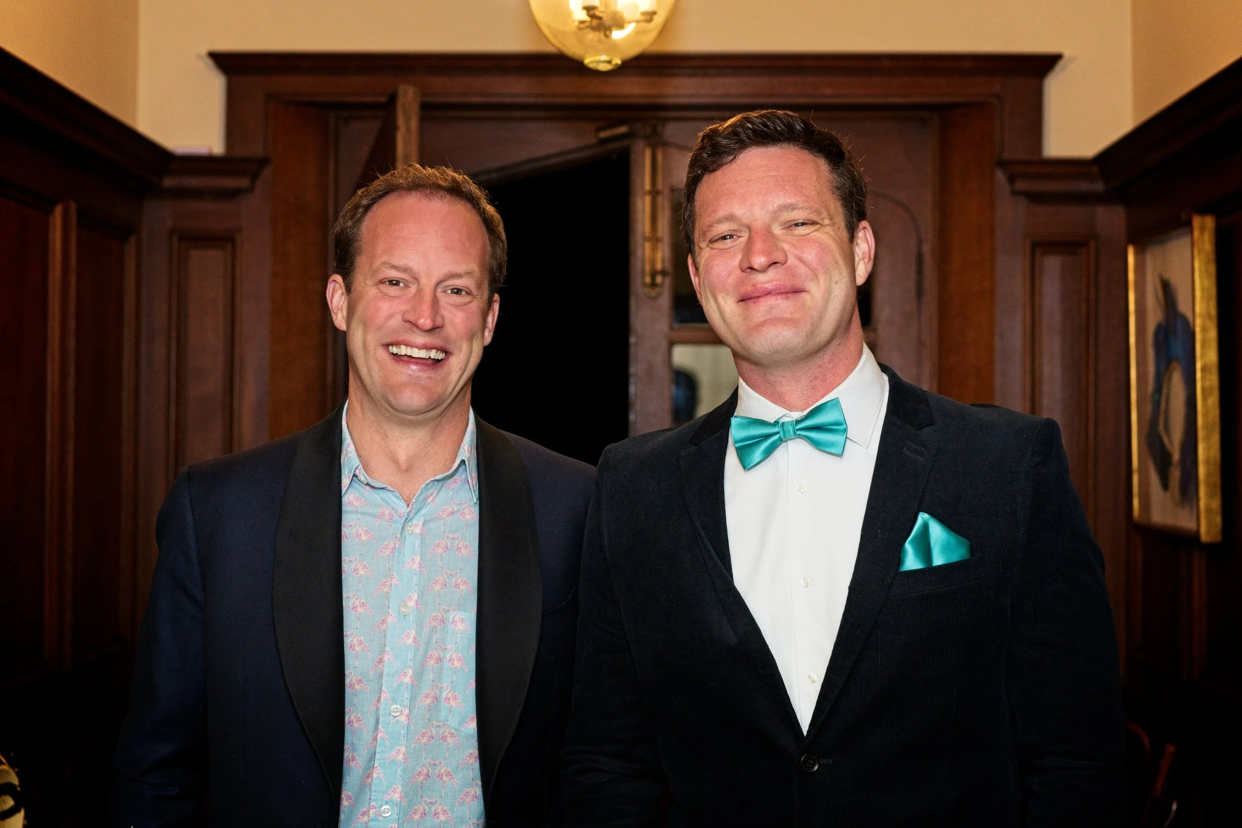 Two men dressed in formal attire smiling indoors, with wooden panelling and artwork visible in the background. Event Photography by photographer based in Southam, Warwickshire.