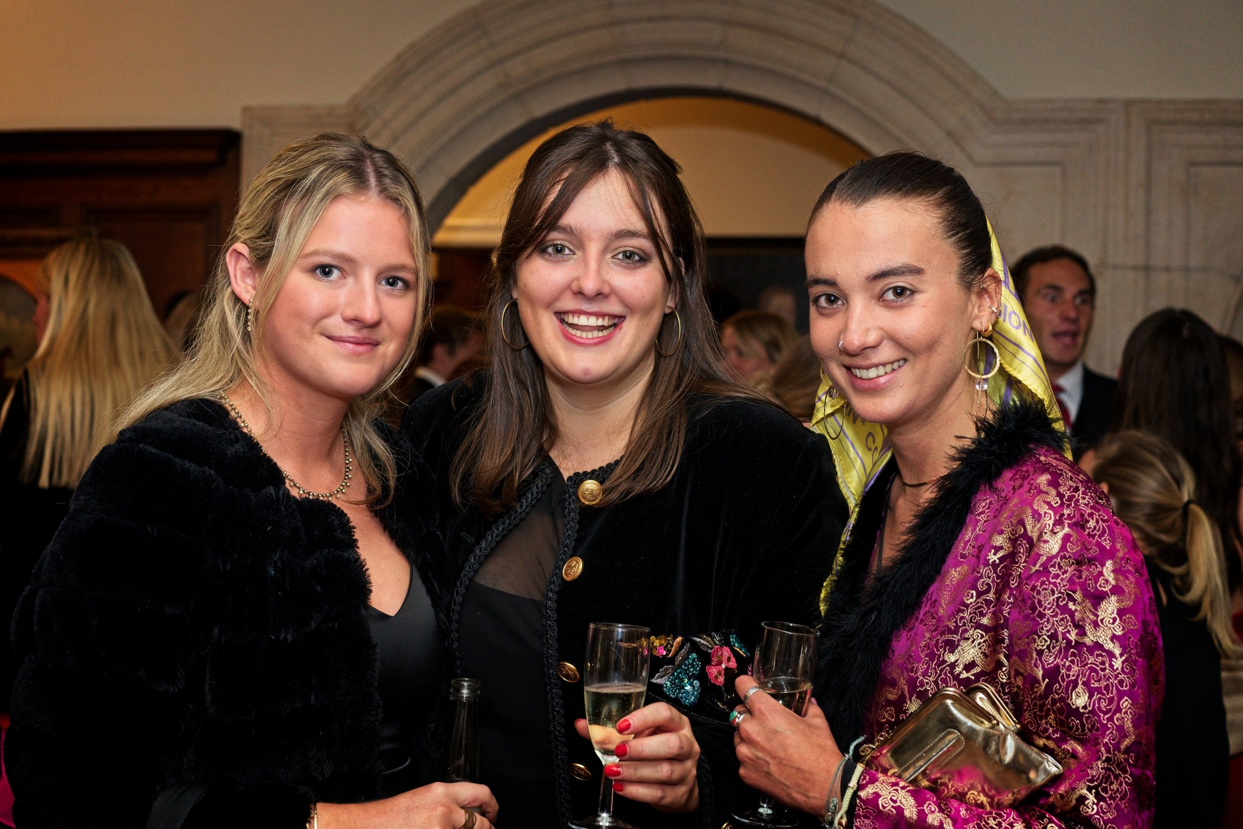 Three women standing together at a social event, holding glasses of champagne and smiling at the camera. Event Photography by photographer based in Southam, Warwickshire.
