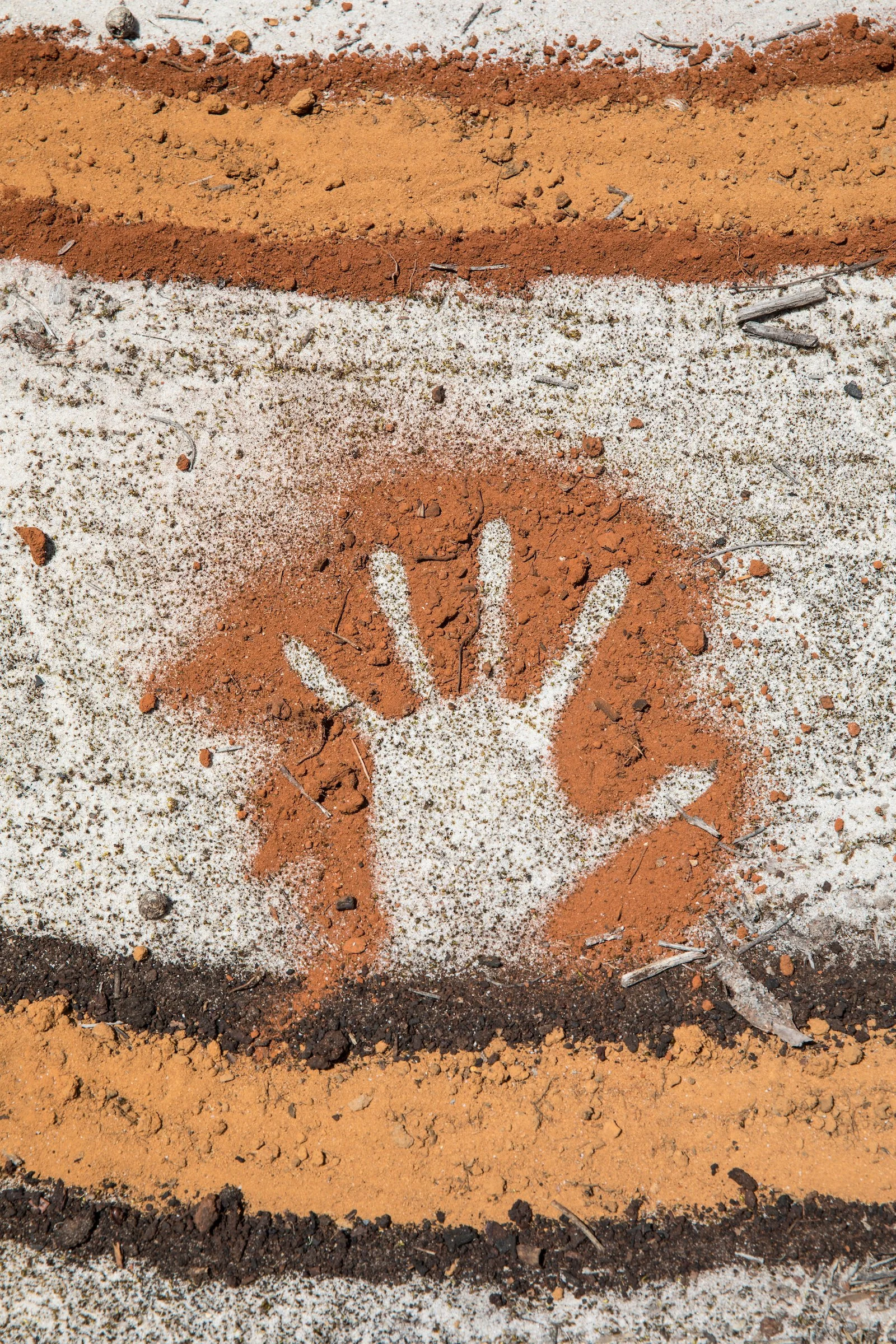 Four layers of different colored soil, with a handprint drawn in the white layer at the bottom.