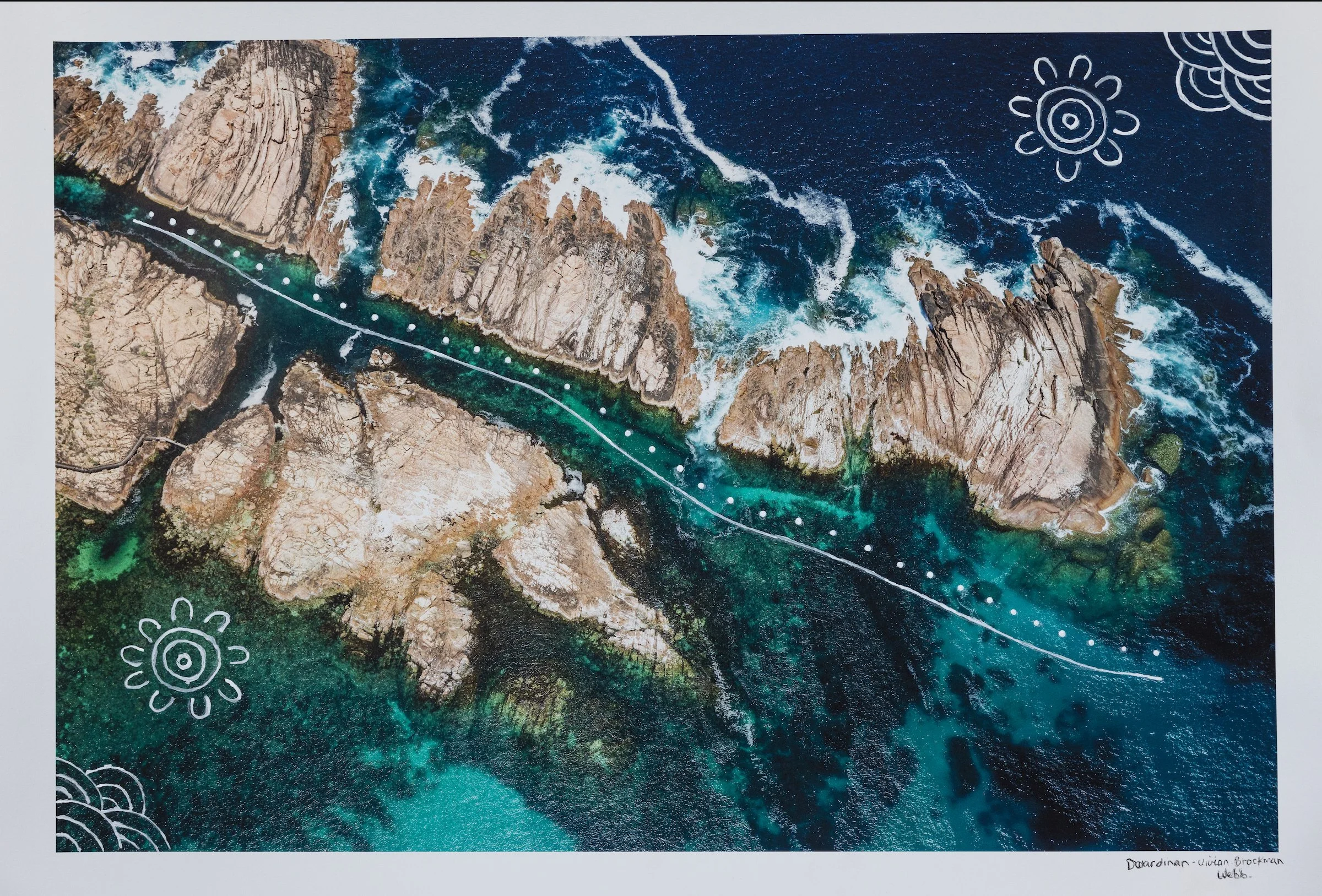 Aerial view of rugged rocky coastline with turquoise water and white foam from crashing waves. Hand-drawn white doodles of sunflowers and waves are overlaid on the image. The bottom right has handwritten text: 'Doodlings - Vivian Brockman, Web'.