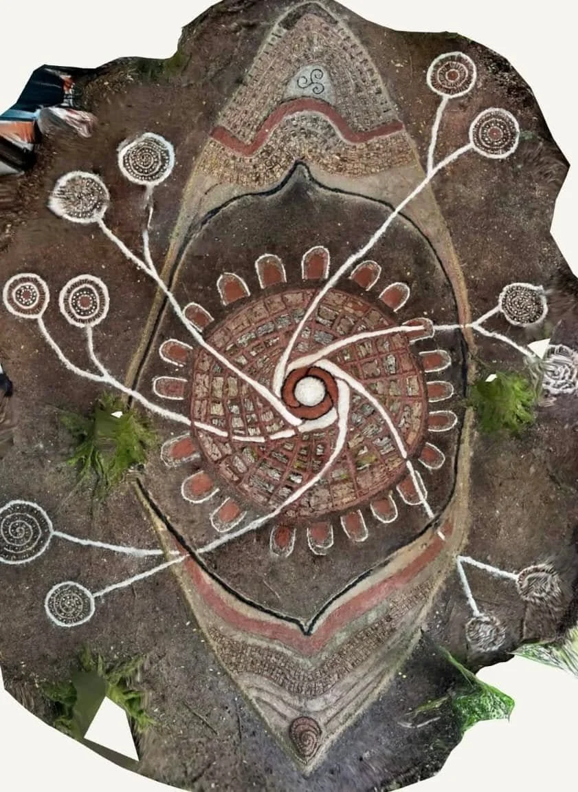 An ancient rock carving featuring spiral patterns, circular designs, and geometric shapes with painted embellishments in red, white, and black. Some green leaves are placed on the carving.