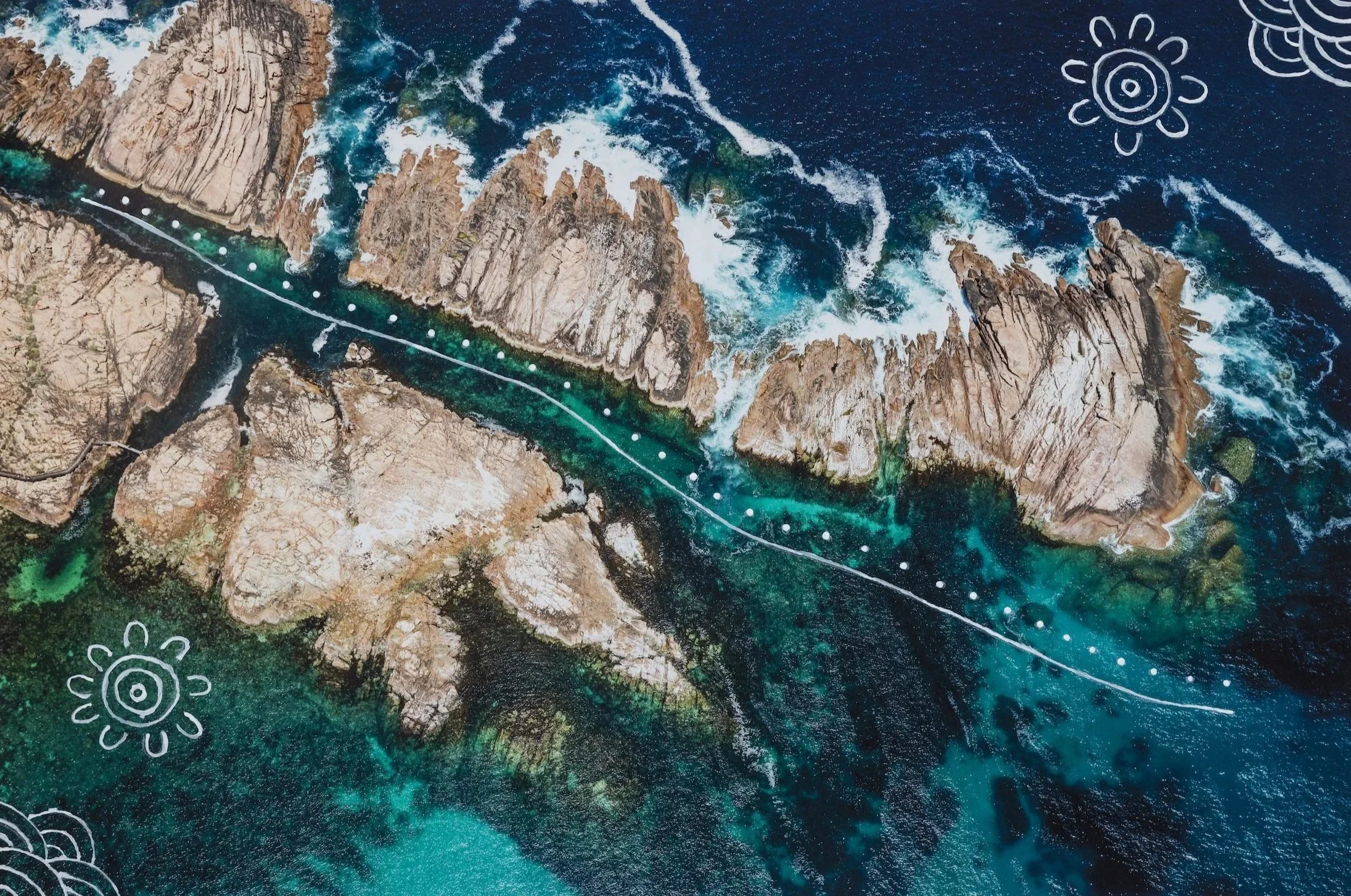Aerial view of rocky coastline with crashing waves and a sandbar across turquoise waters, decorated with white doodles of suns and clouds.