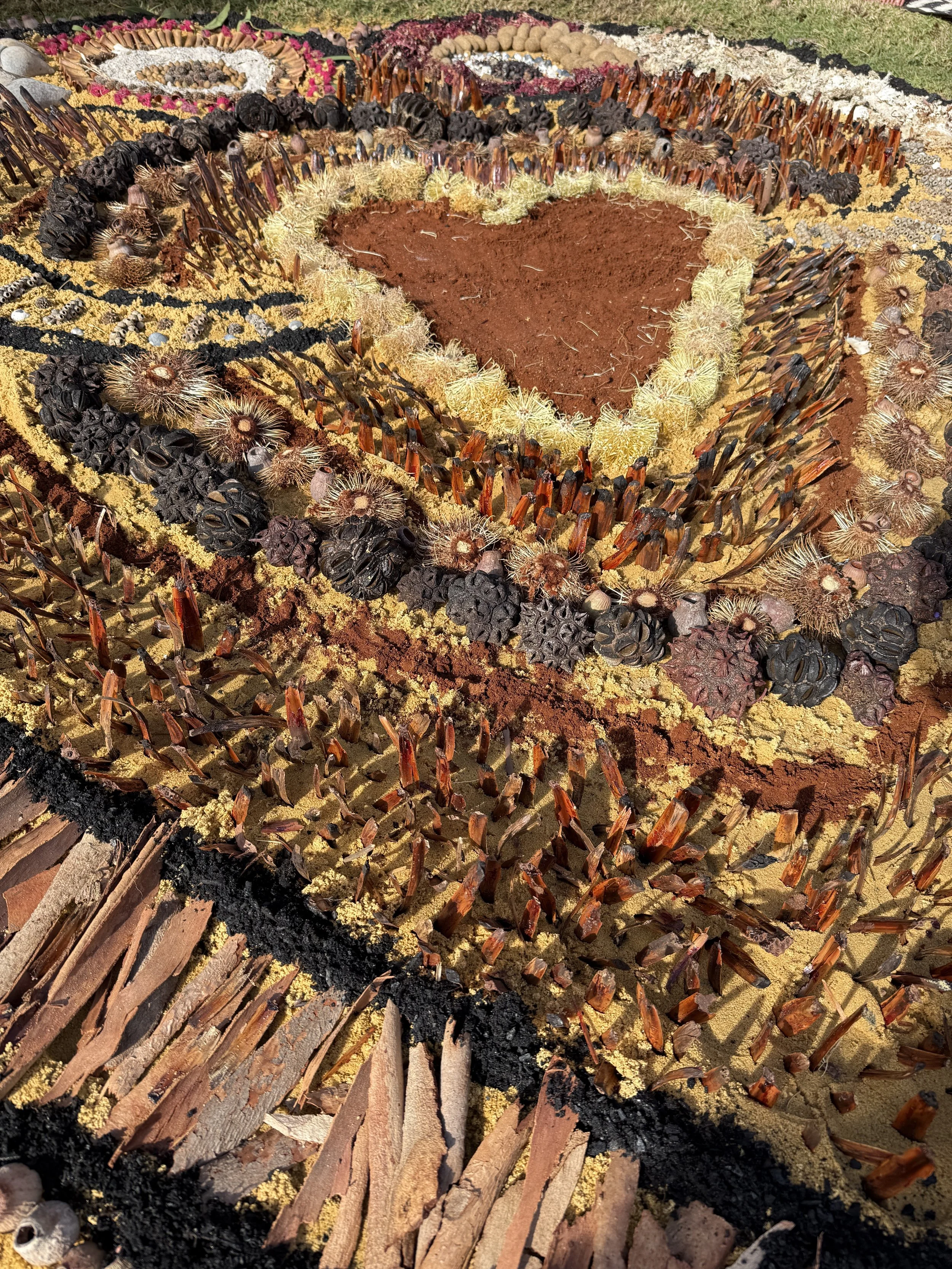 A large, colorful, artistic mosaic made from natural materials such as bark, seeds, and dried plants, arranged to form various patterns and shapes.