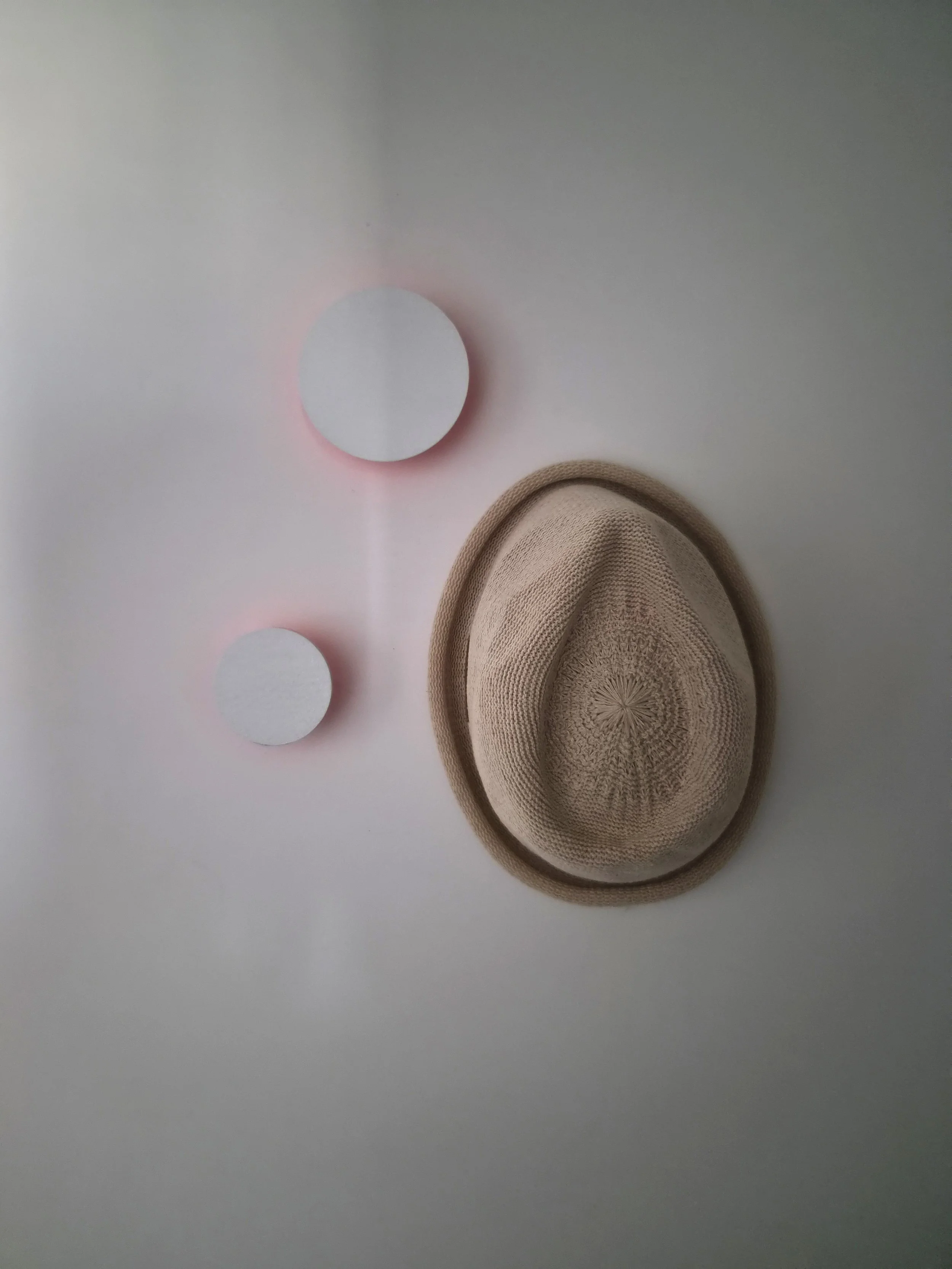 Un cappello di paglia beige poggiato su una superficie bianca, con due luci rotonde di riflesso.