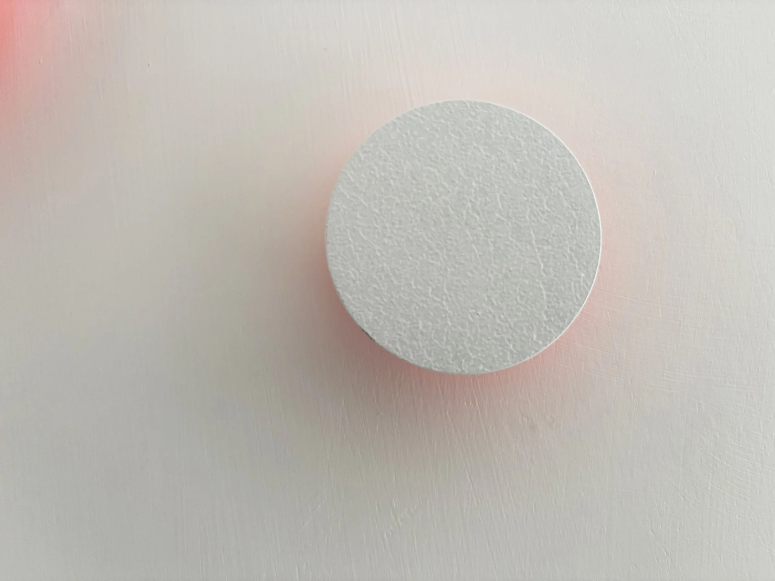 Una pallina bianca di tecno in rilievo su una superficie di colore rosa chiaro.