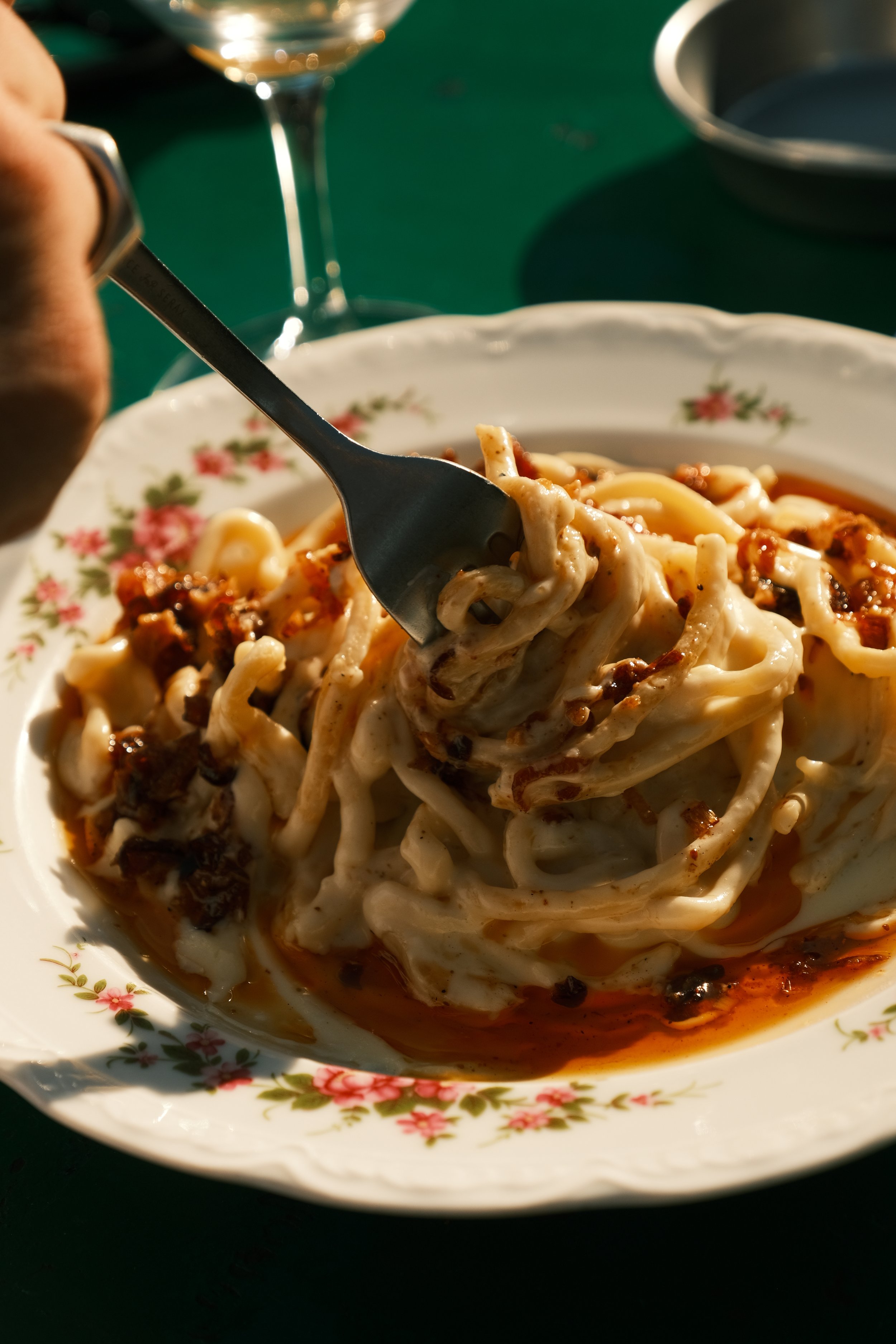 Close-up of a white floral patterned bowl filled with spaghetti, topped with tomato sauce and ground meat, with a fork lifting some noodles.