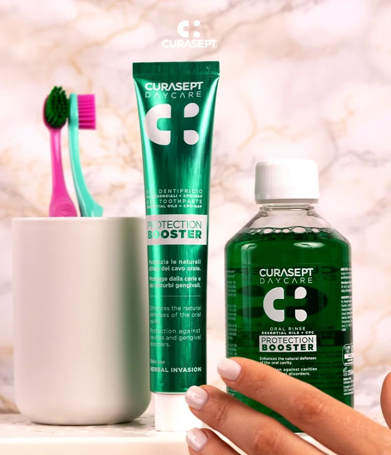 Prodotti per l'igiene orale: due spazzolini e due flaconi di collutorio e dentifricio CuraSept, tutti di colore verde, disposti su un piano con sfondo di marmo chiaro
