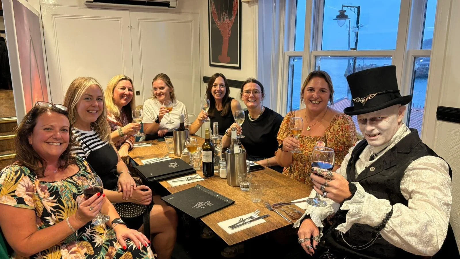 Group of women and a person in Victorian costume enjoying drinks at a dinner table in a restaurant. Vlad Dracul III - Dracula Personal Appearance for a 50th Birthday party in Magpie Café, Whitby
