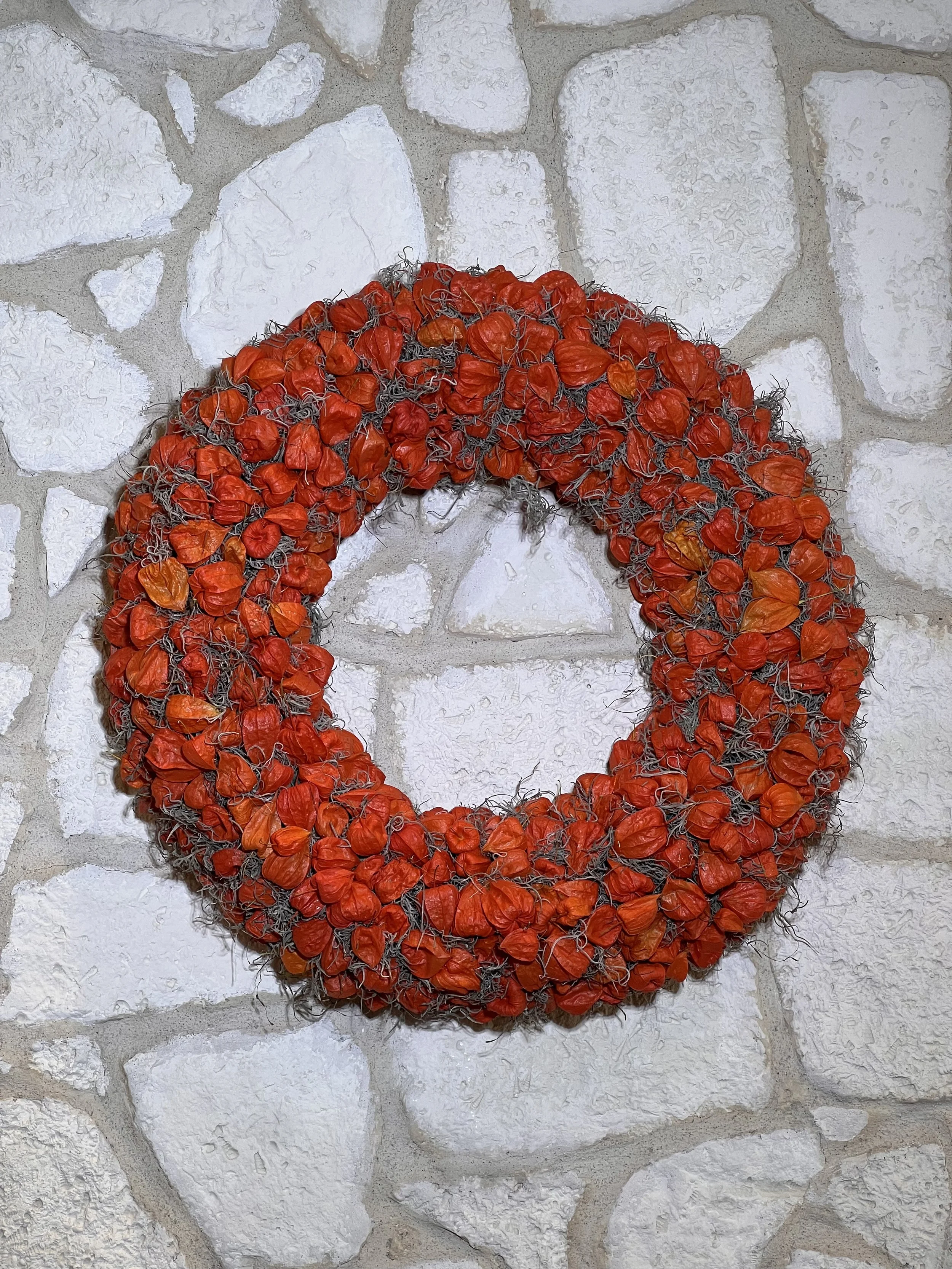 Runder Herbstkranz aus orangefarbenen Physalis vor einer hellen Steinwand.