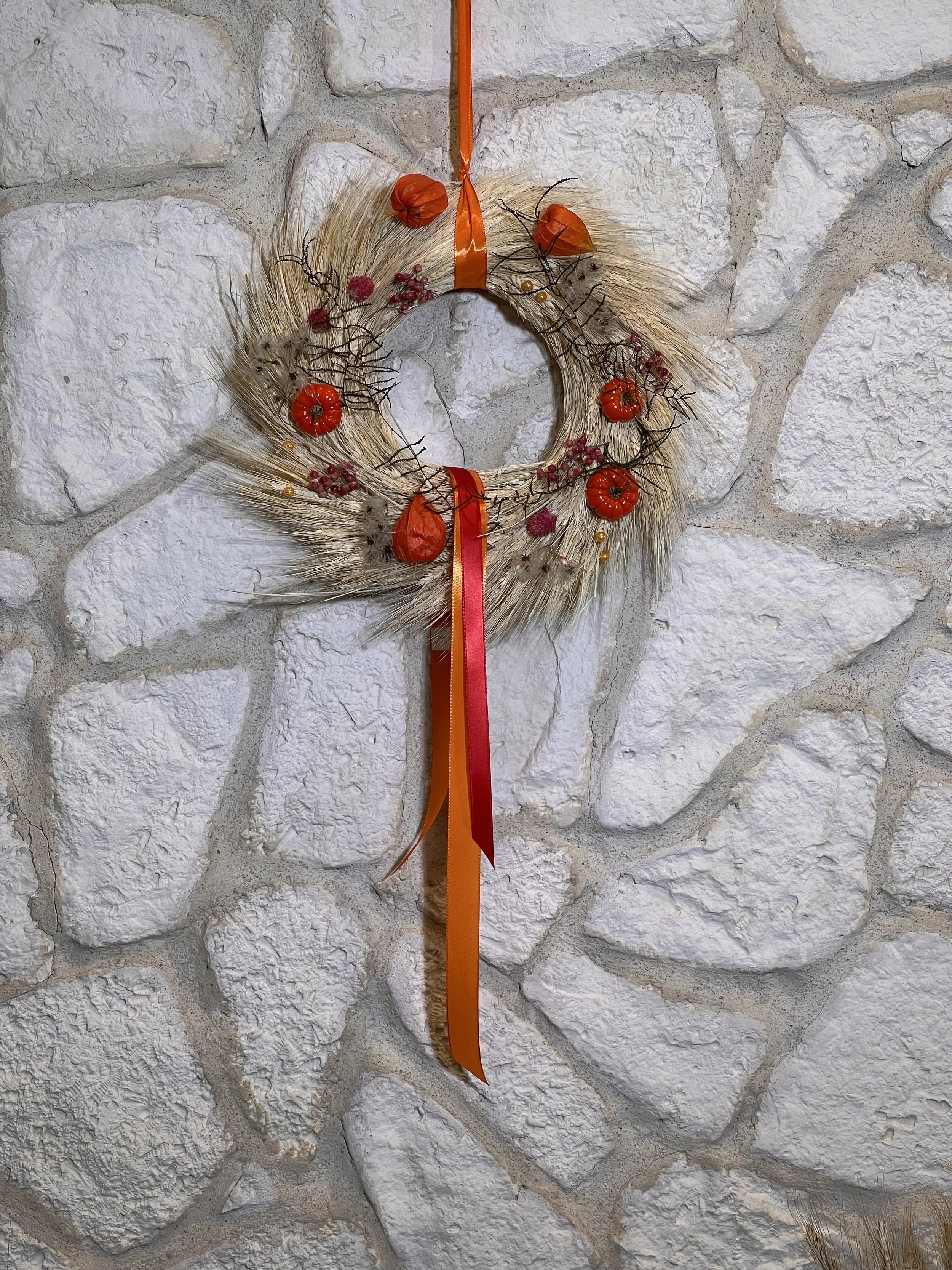 Herbstkranz aus Ähren mit Physalis, roten Akzenten und langen orangefarbenen Bändern.
