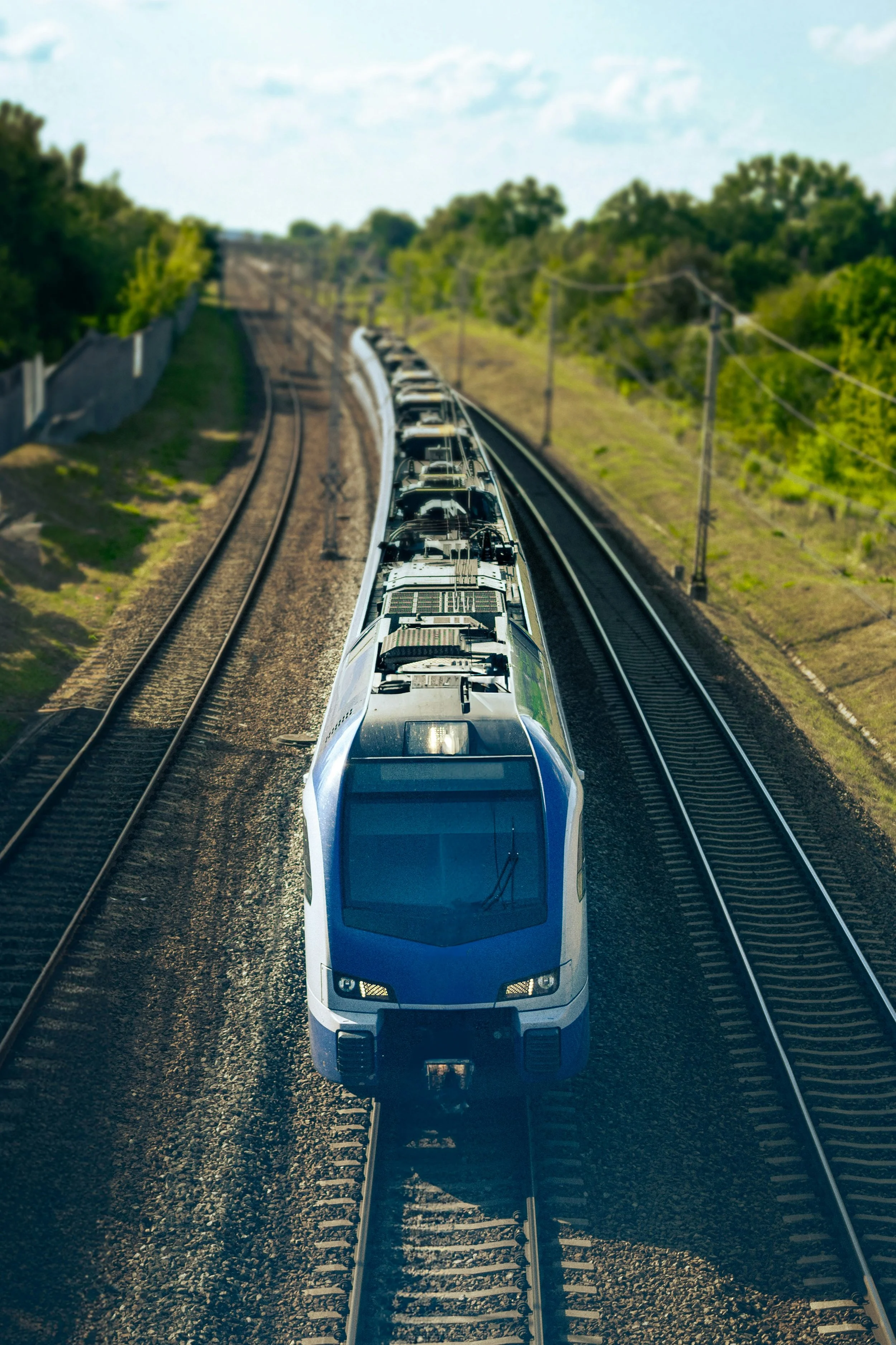 Un train à grande vitesse noir et blanc circulant sur une voie ferrée à double voie, avec un paysage verdoyant et un ciel partiellement nuageux en arrière-plan.