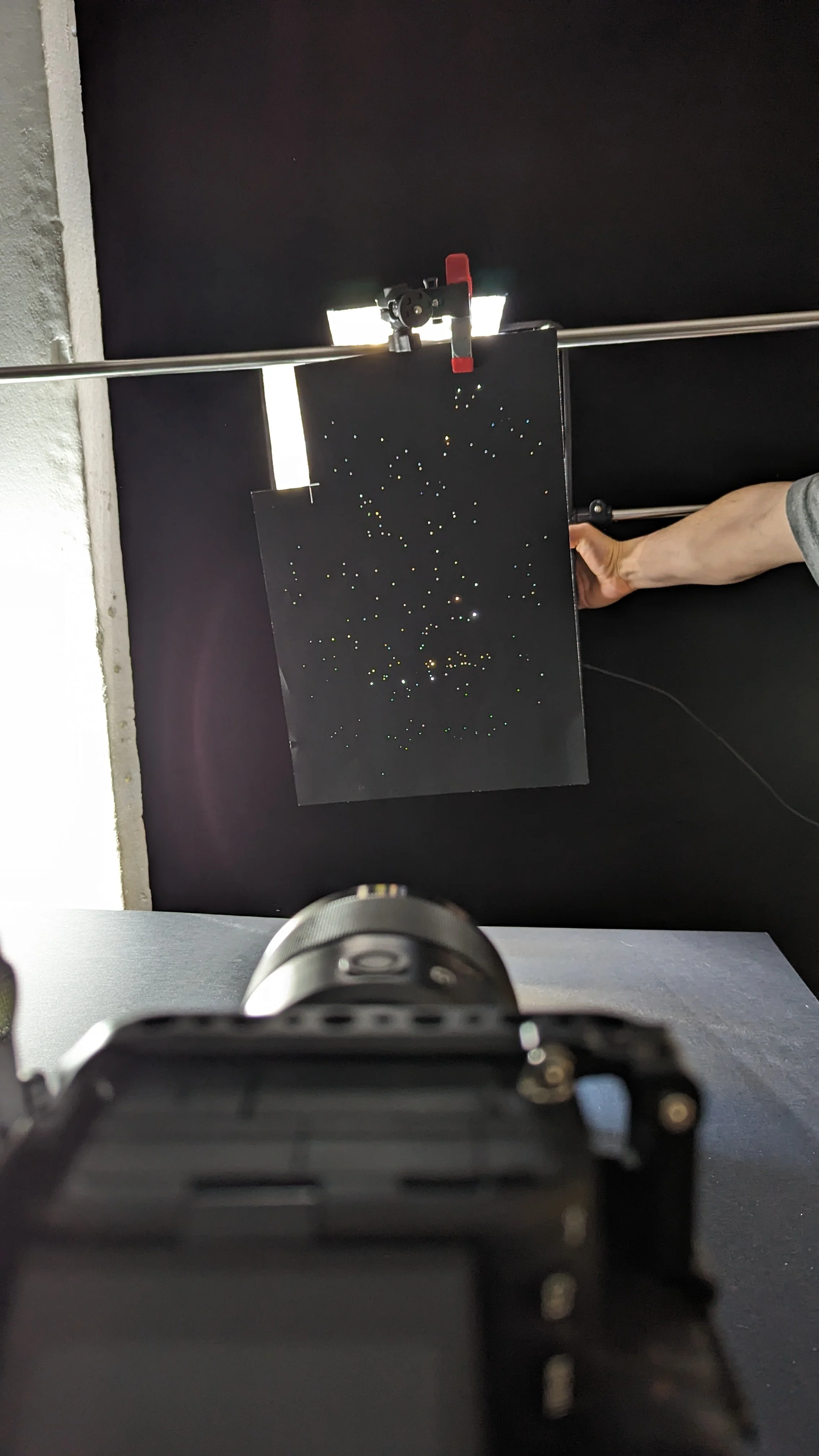 Immagine di un telescopio puntato verso un pannello nero con punti luminosi che rappresentano le stelle, visibile in un ambiente scuro.