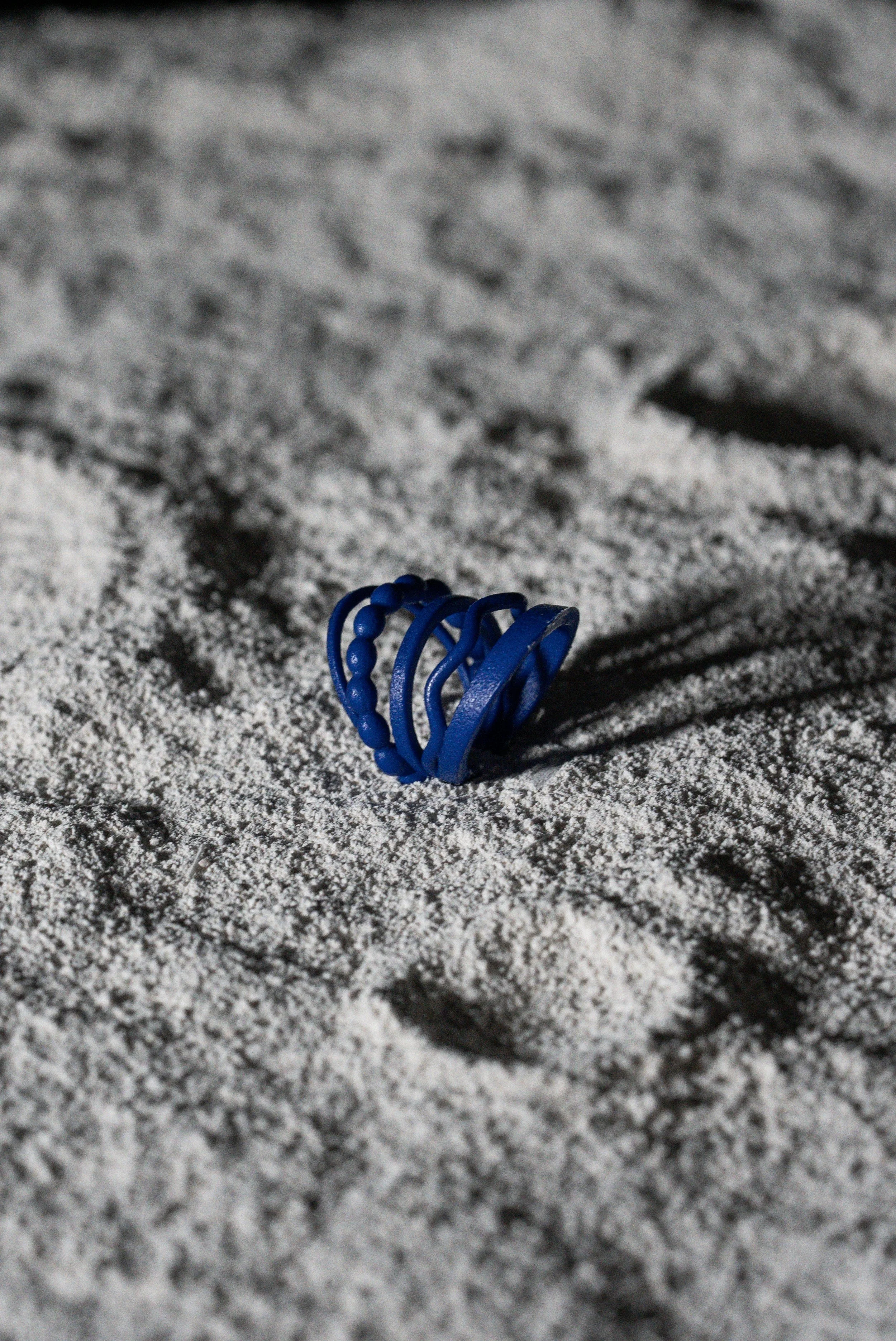 Un anello blu di plastica con un design articolato si trova sul terreno di sabbia.
